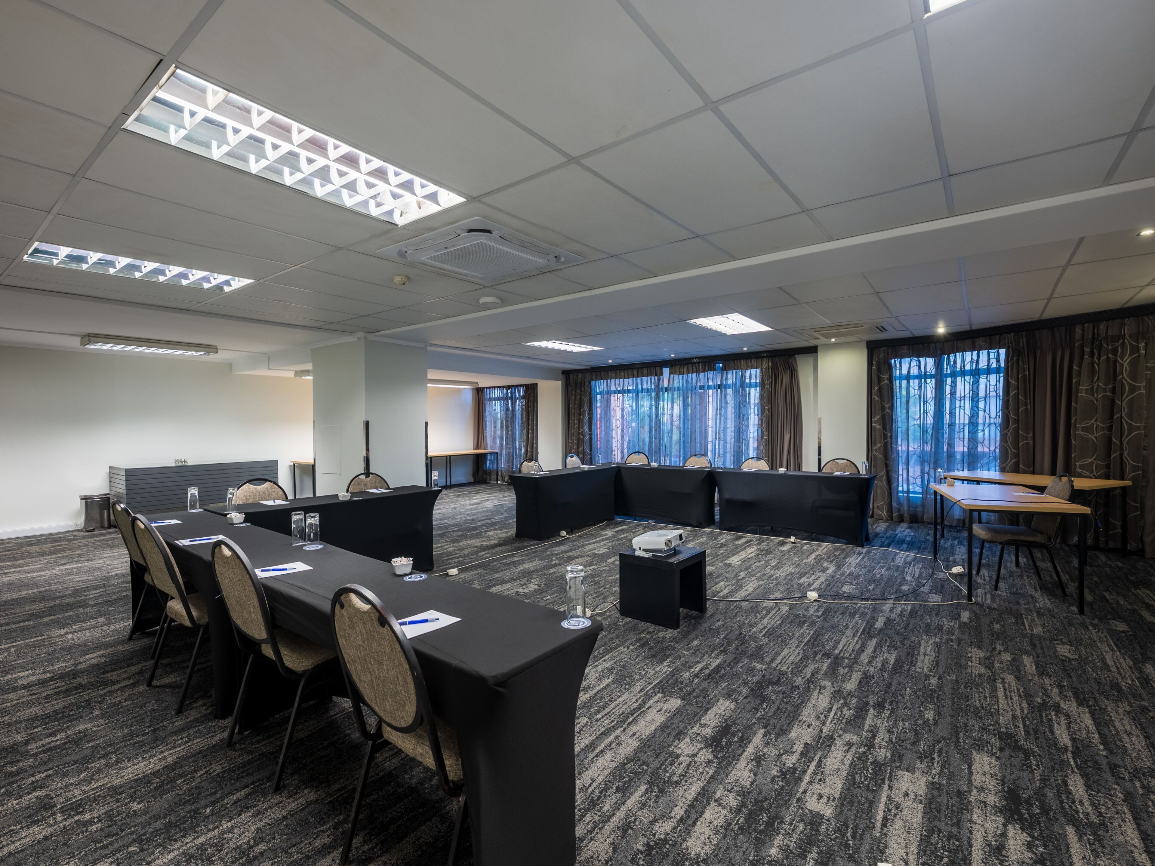 Un salón de conferencias con una larga mesa, sillas, un proyector y piso alfombrado.
