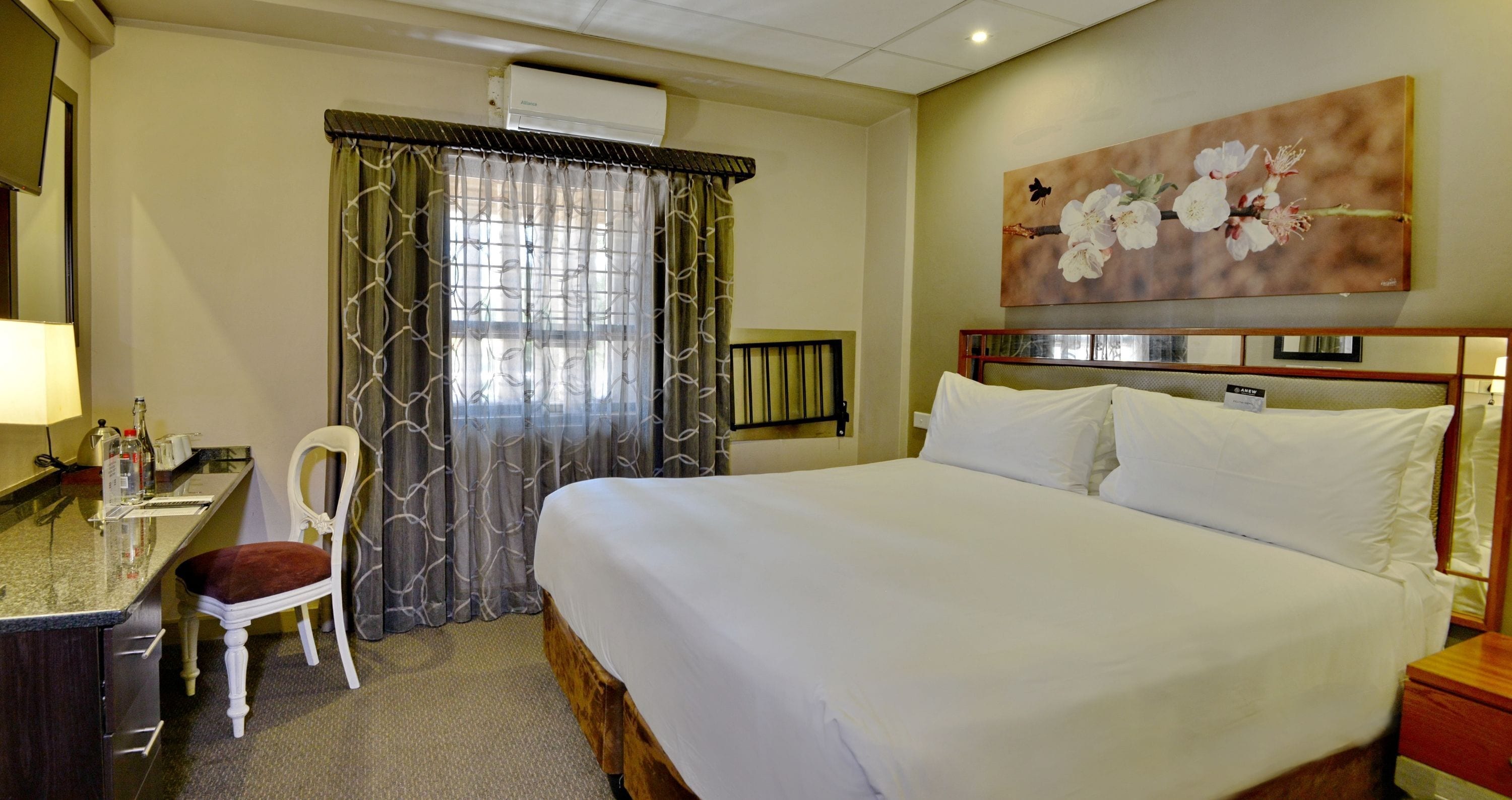 Ein Hotelzimmer mit einem Bett, einem Schreibtisch, einem Sessel und einem Gemälde an der Wand.