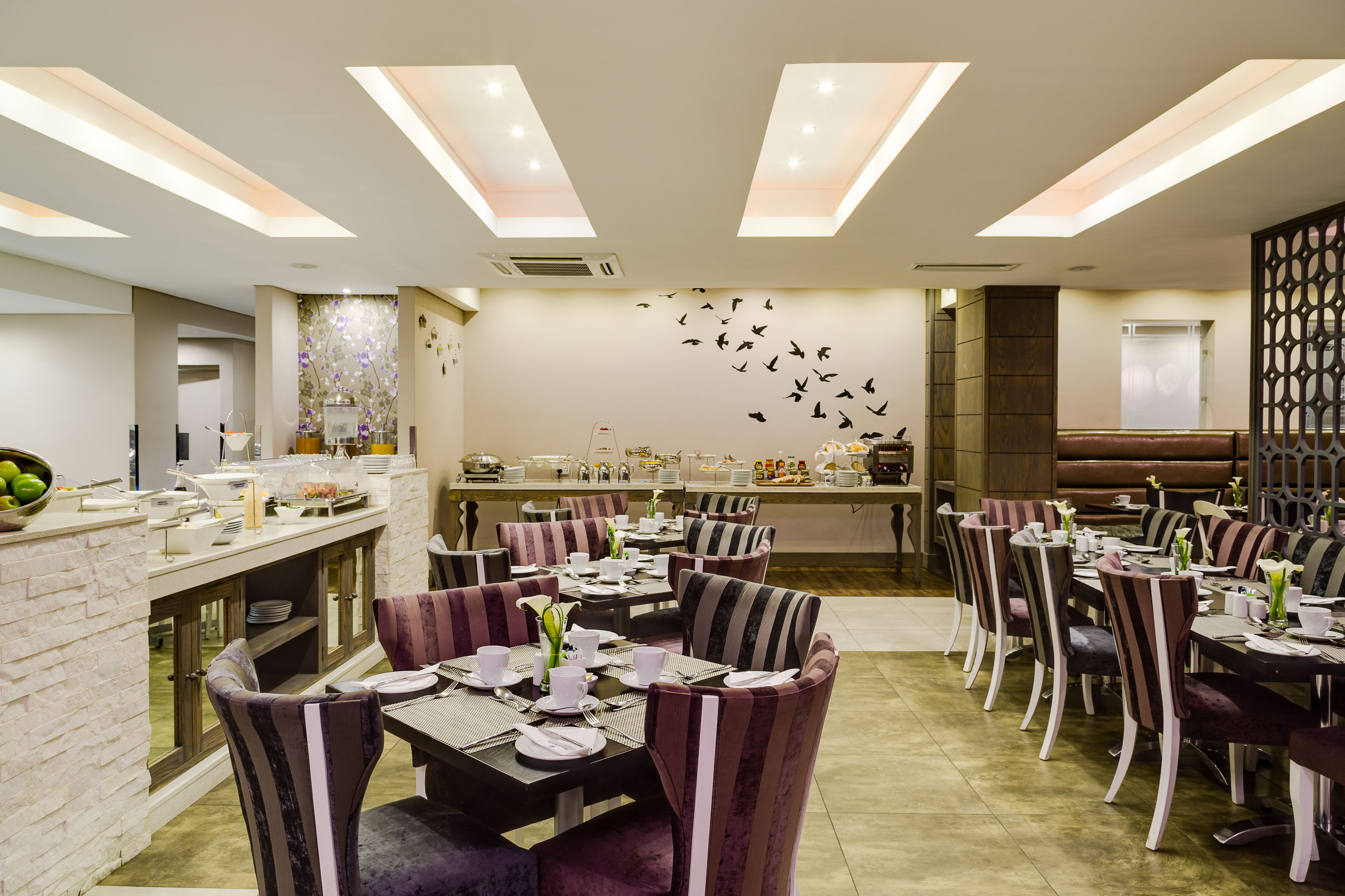 Un restaurante con varias mesas y sillas, una zona de bar y una pared decorada con un mural de aves.