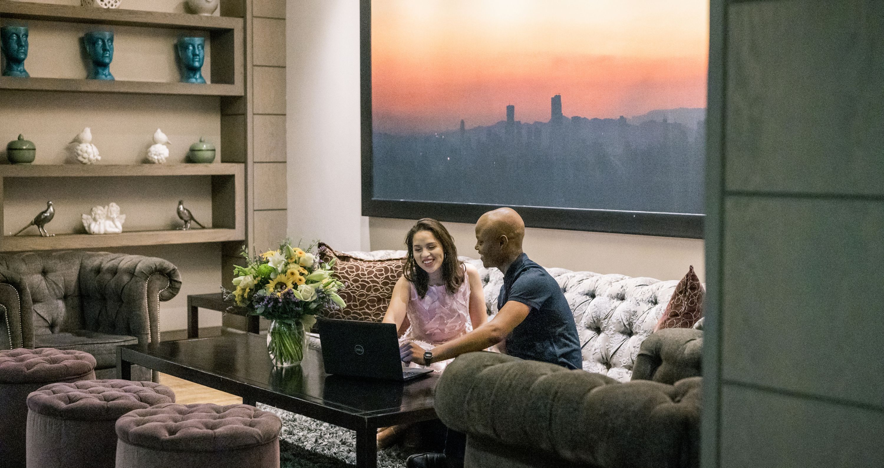 Ein Wohnzimmer mit Blick auf die Stadt, ein Sofa, ein Couchtisch mit einem Laptop und dekorative Gegenstände auf Regalen.