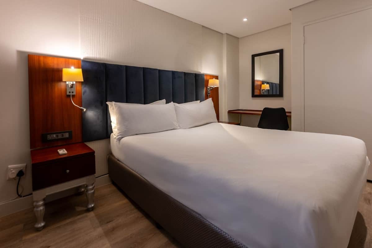 Une chambre d’hôtel avec un grand lit, une table de chevet en bois, un bureau et un miroir au mur.
