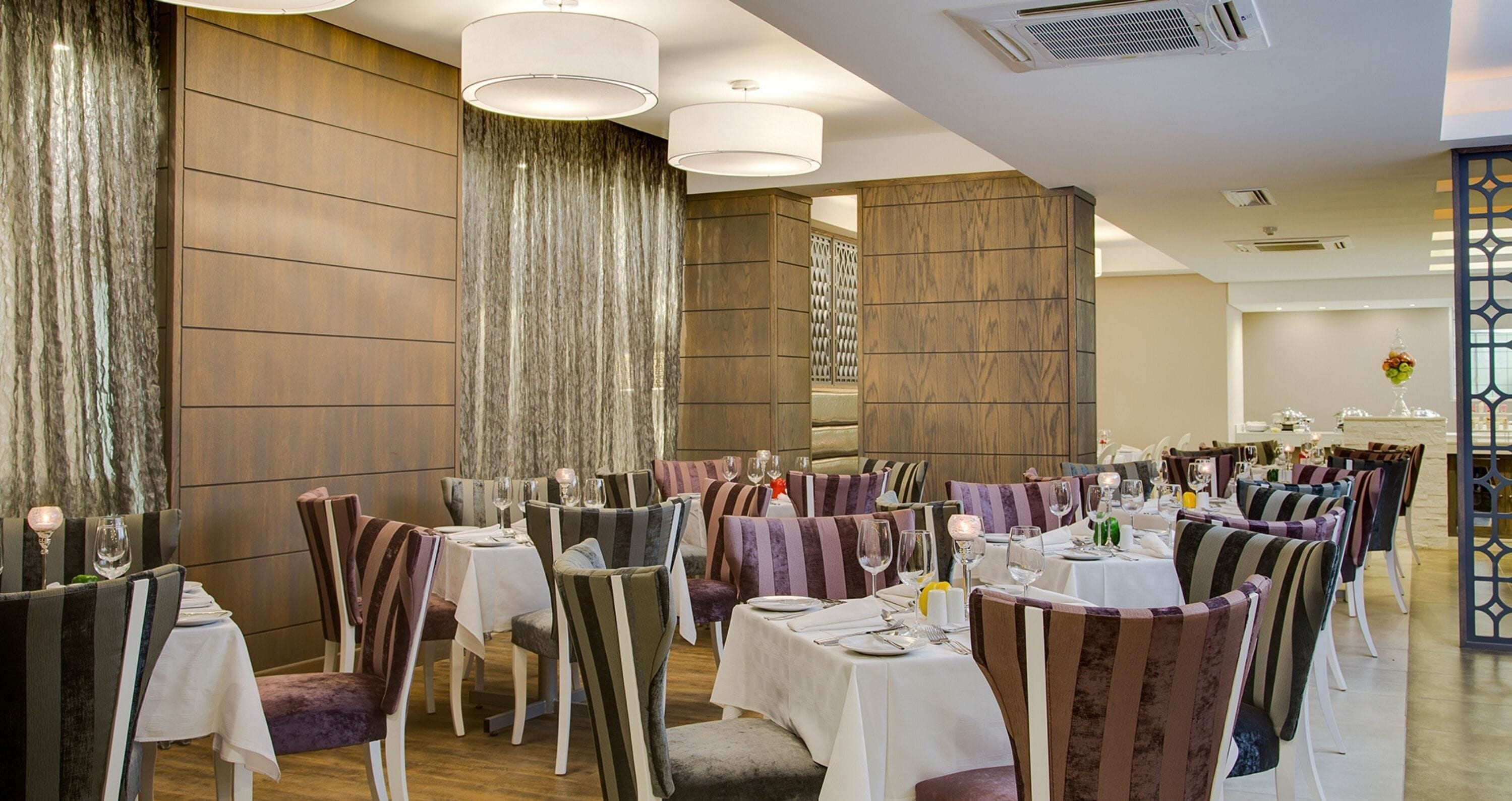 Een restaurant met meerdere tafels en stoelen, elk voorzien van een witte tafelkleed en wijnglazen.