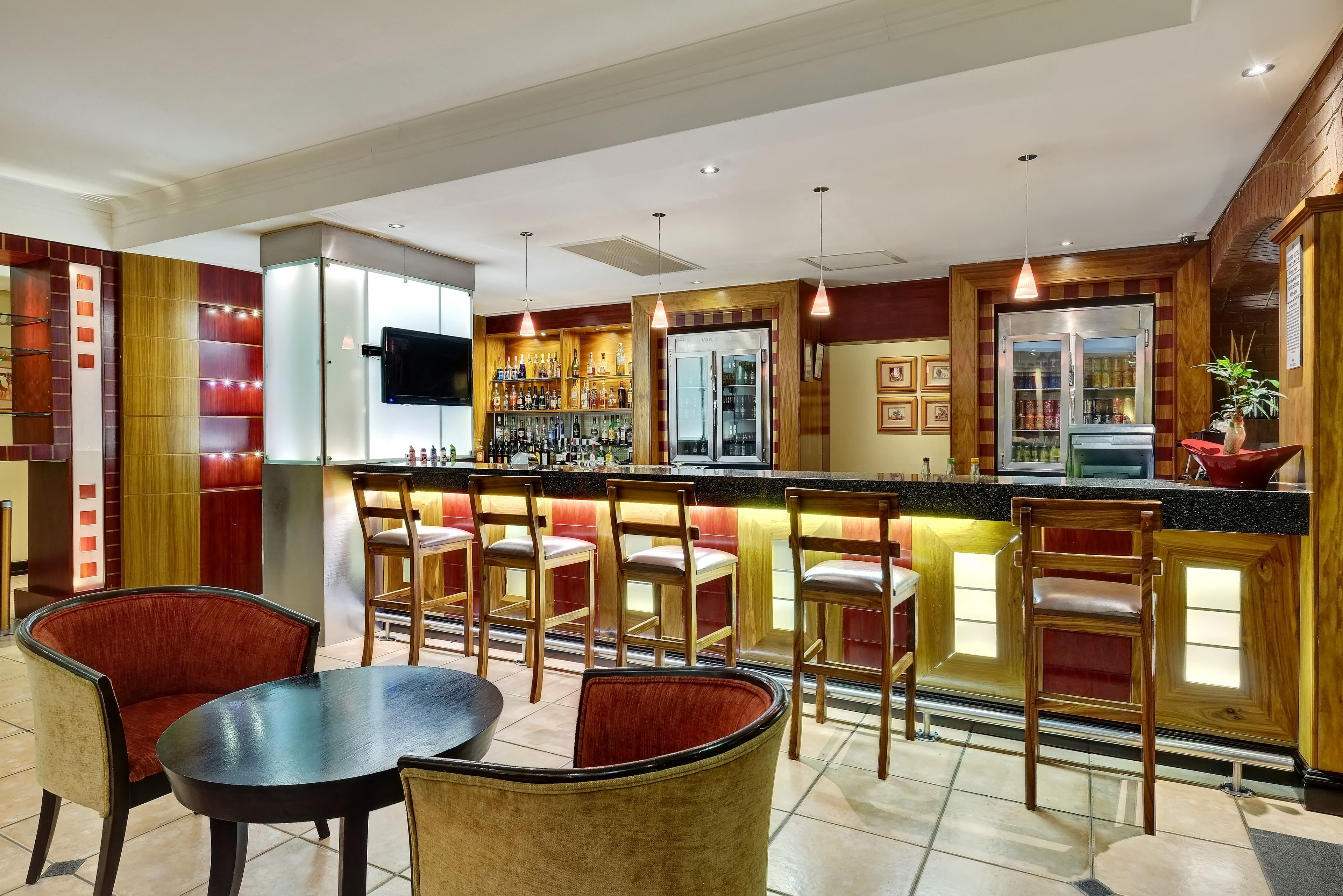Eine Bar mit einer Theke, mehreren Barhocker und einem Fernsehbildschirm.