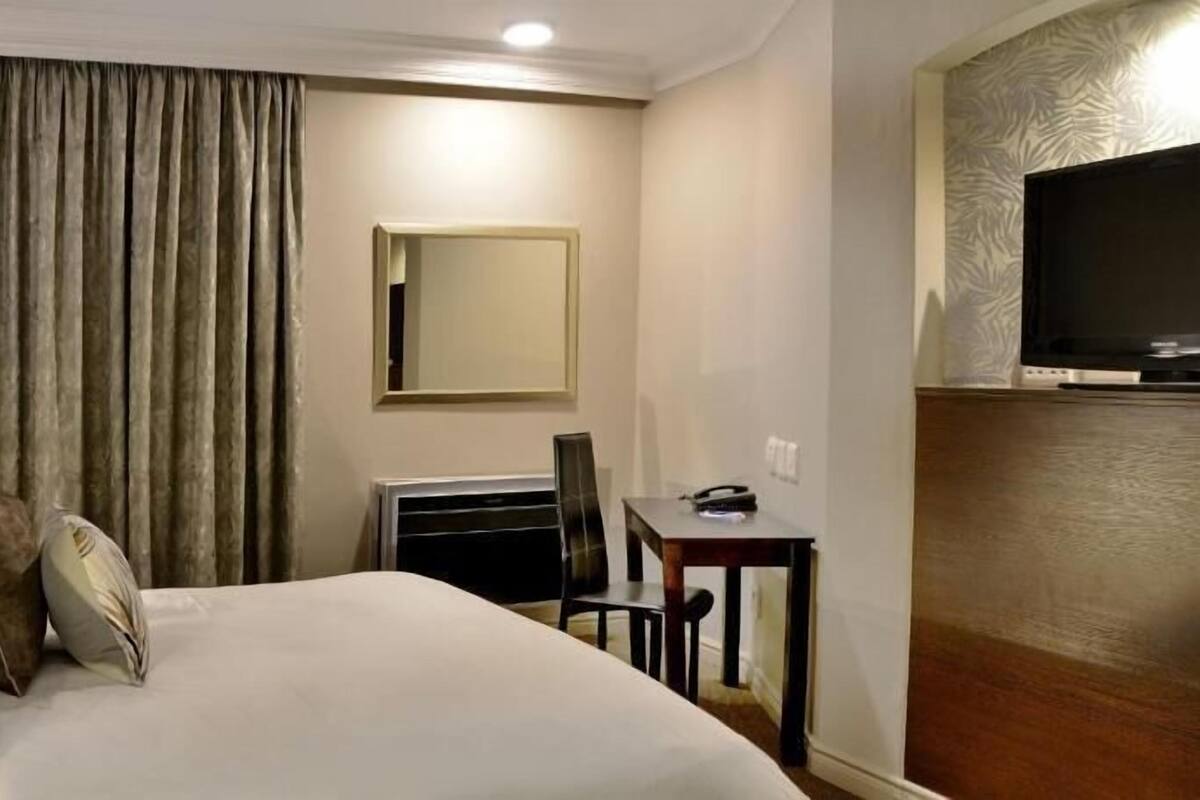 A hotel room with a bed, a desk, a chair, a television, and a large window with curtains.
