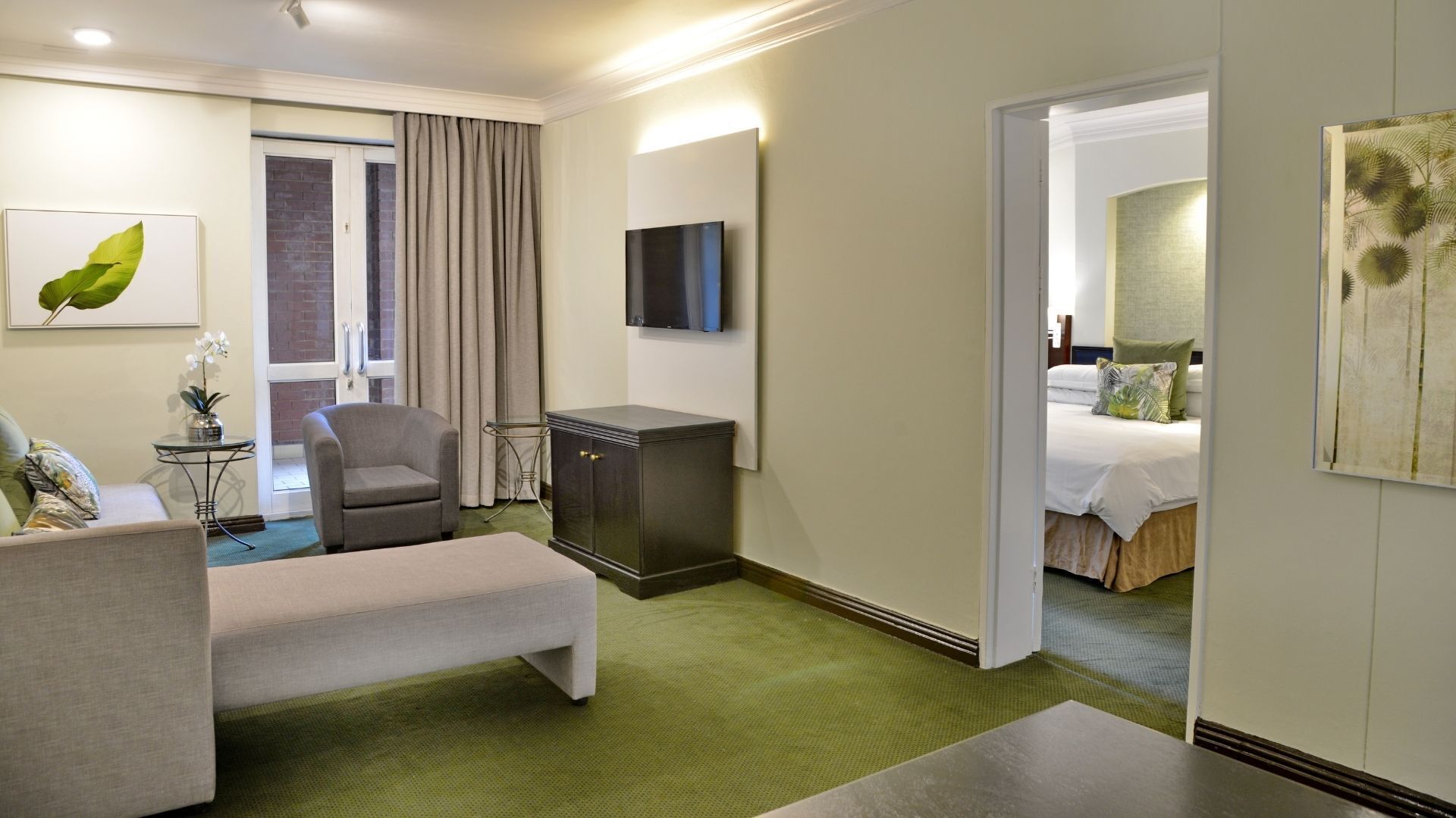 Ein Hotelzimmer mit einem Bett, einem Schreibtisch, einem Sessel, einem Fernseher und einer Tür zu einem anderen Raum.