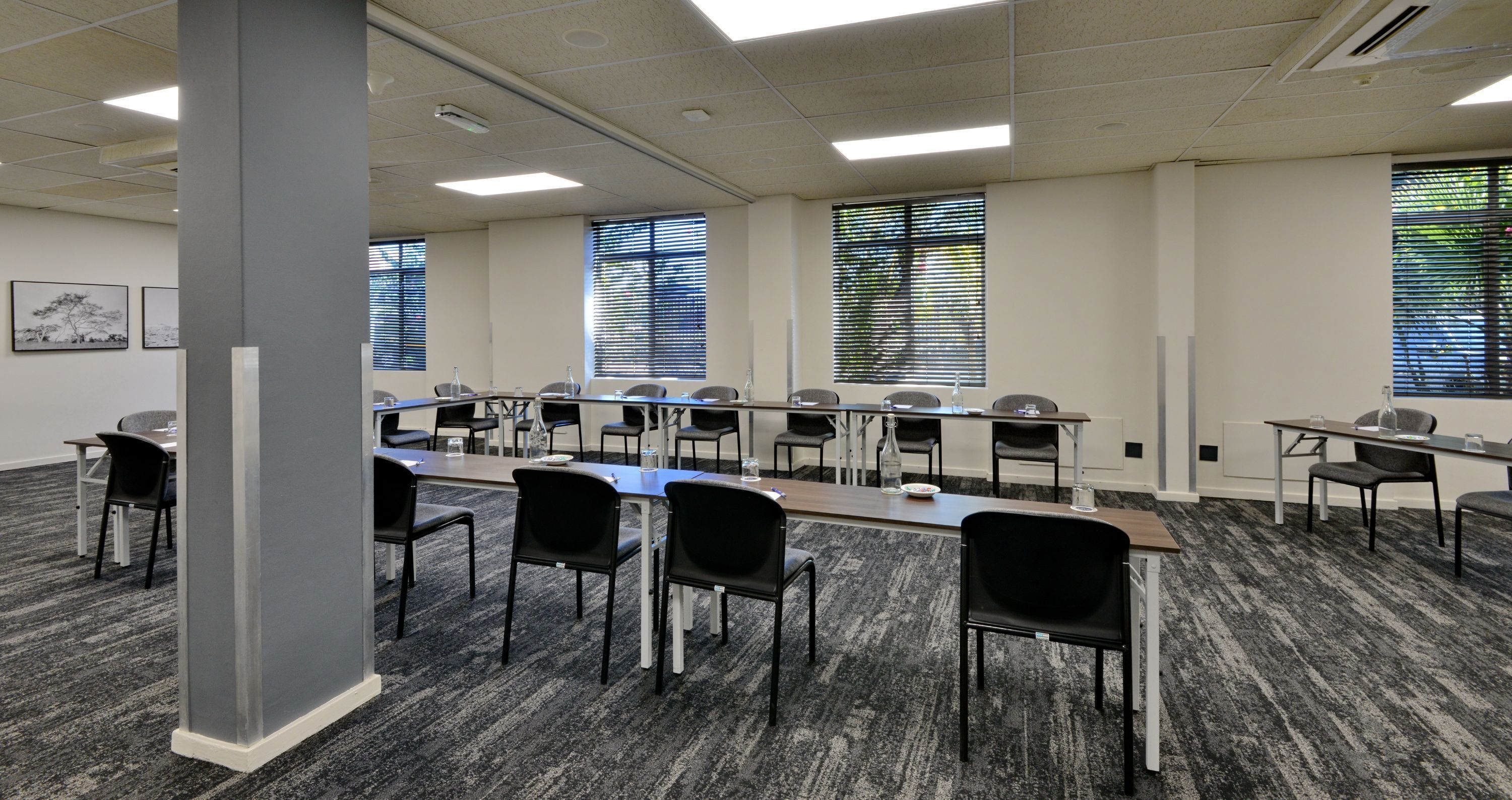Ein Konferenzraum mit einem langen Tisch, mehreren Stühlen und großen Fenstern mit Jalousien.