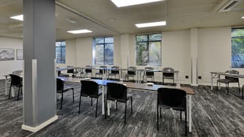Ein Konferenzraum mit einem langen Tisch, mehreren Stühlen und großen Fenstern mit Jalousien.