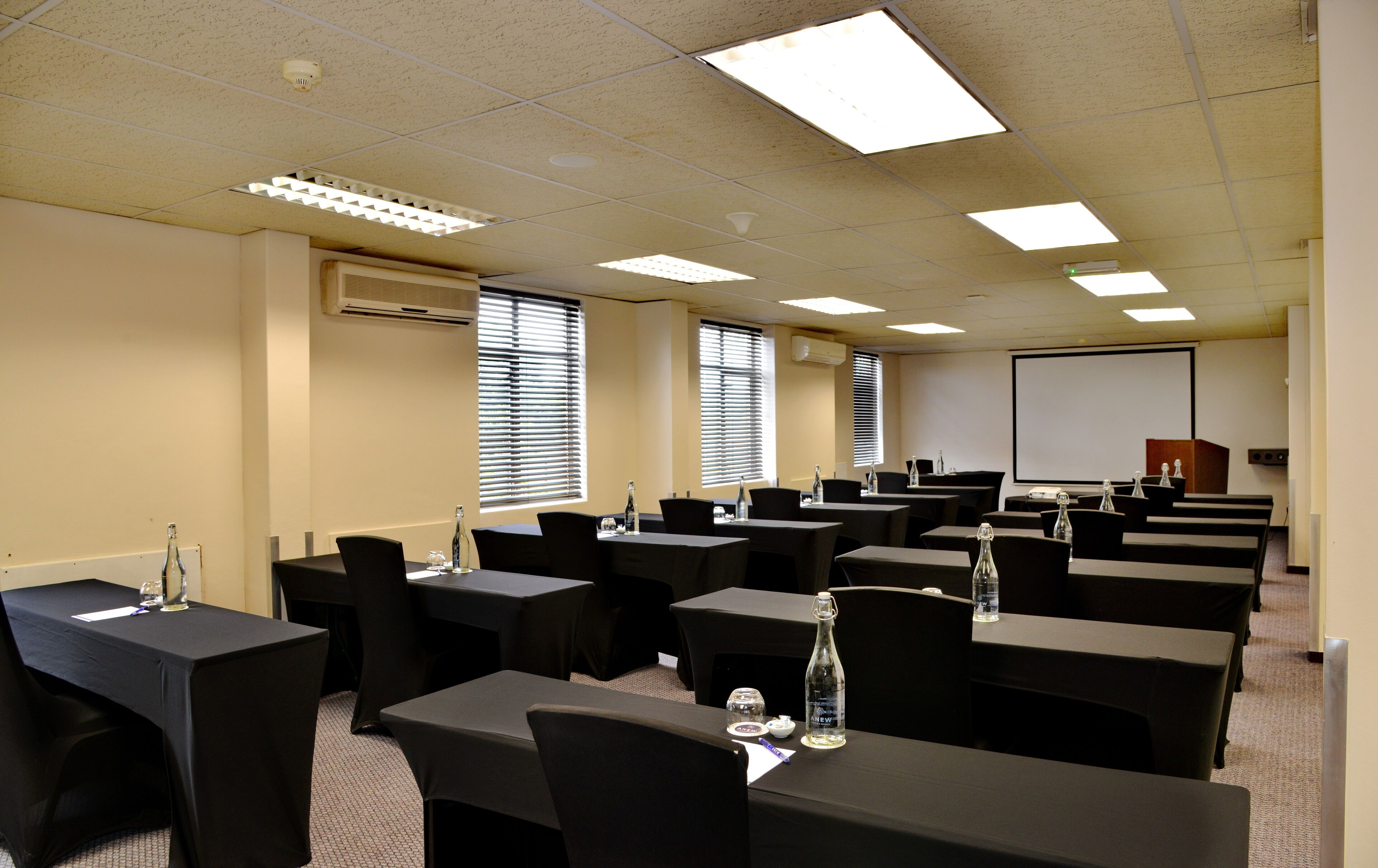 Une salle de conférence équipée de tables et de chaises, de climatiseurs et d’un écran de projection.
