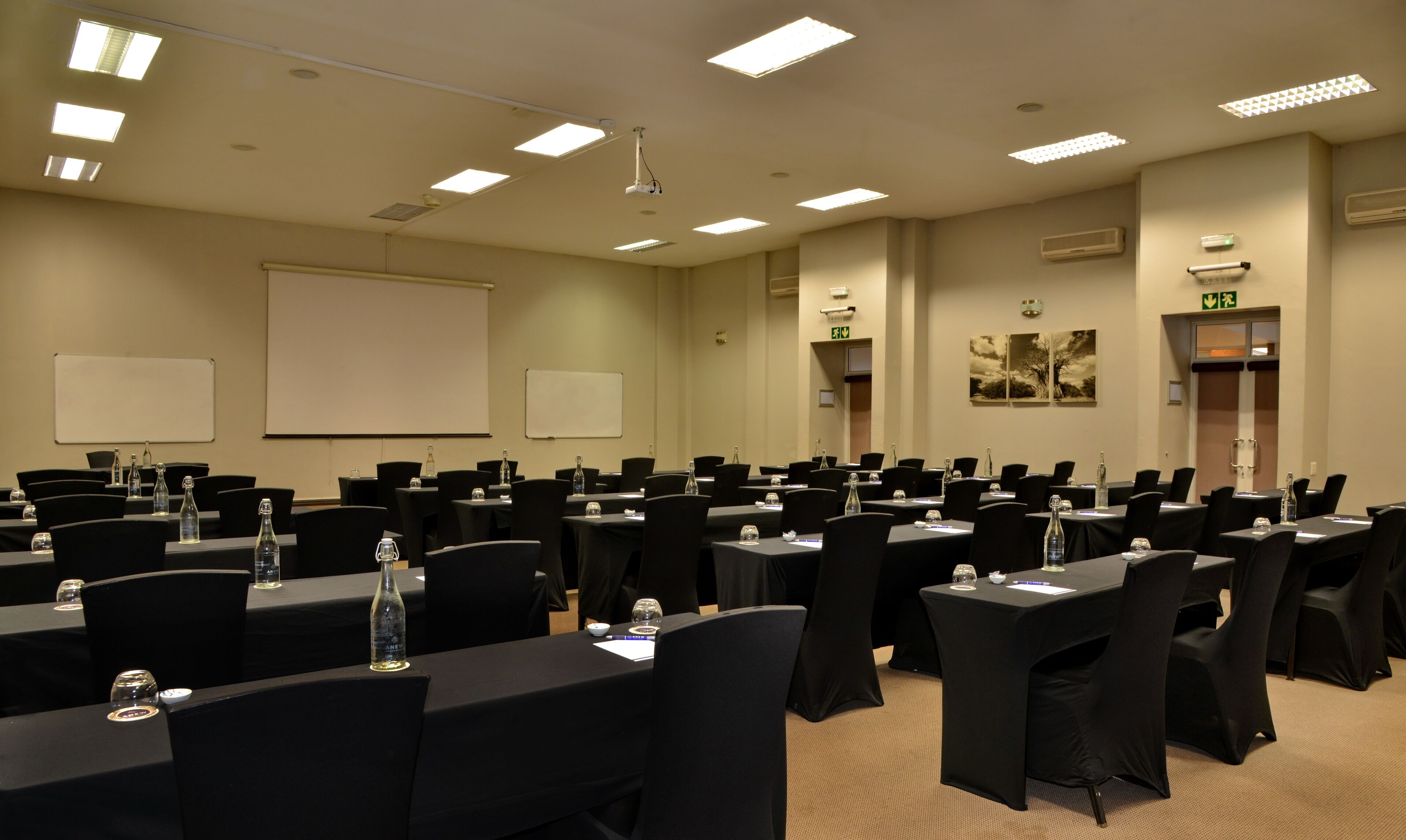 Une salle de conférence dotée de plusieurs tables et de chaises, ainsi que de projecteurs et d’écrans.