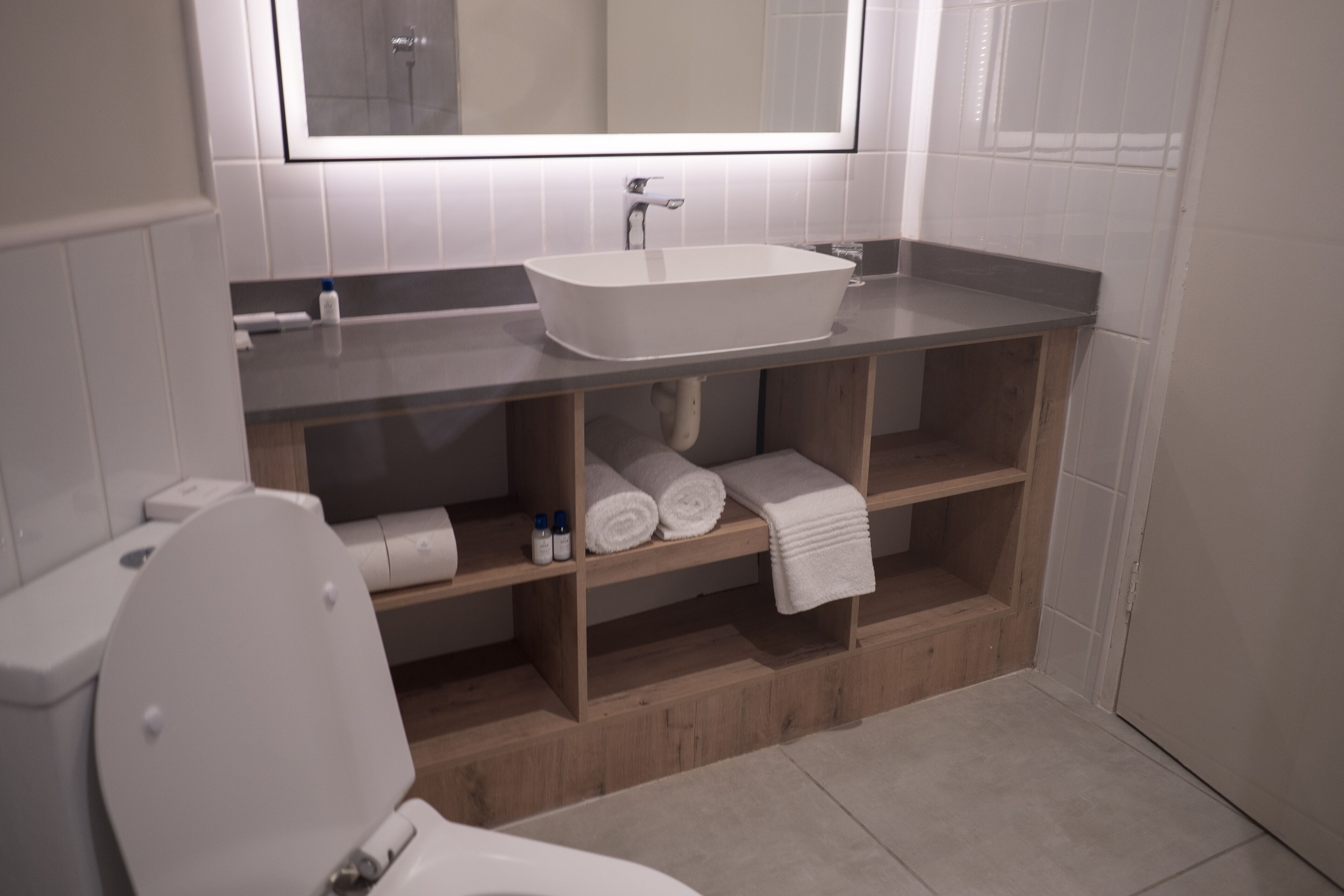 A modern bathroom with a freestanding bathtub, a toilet, and a shelf with towels and toiletries.