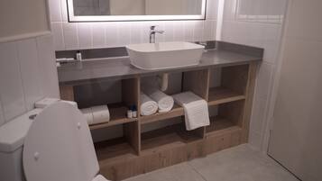 A modern bathroom with a freestanding bathtub, a toilet, and a shelf with towels and toiletries.