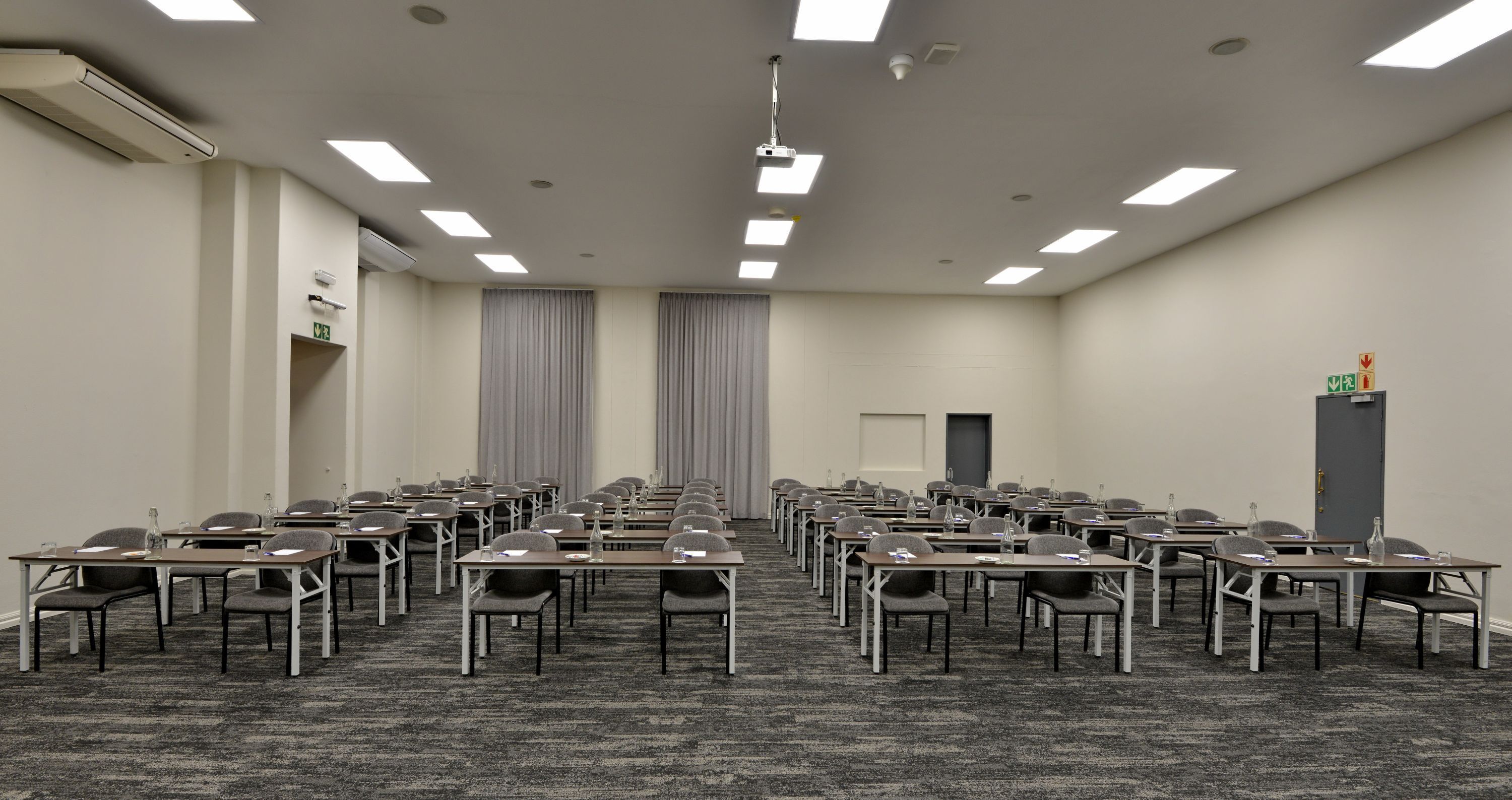 A conference room with rows of tables and chairs, a projector, and a door.