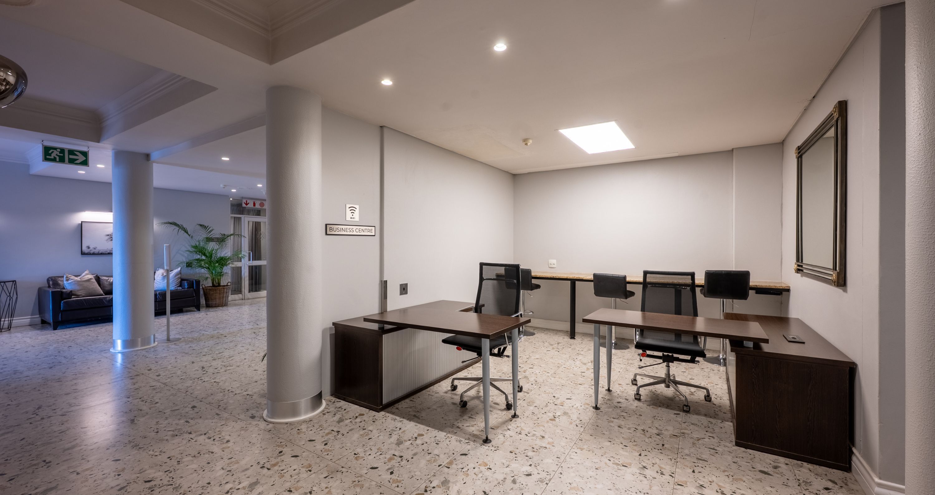 Un moderno centro de negocios con mostrador de recepción, dos puestos de trabajo y un espejo grande en la pared.