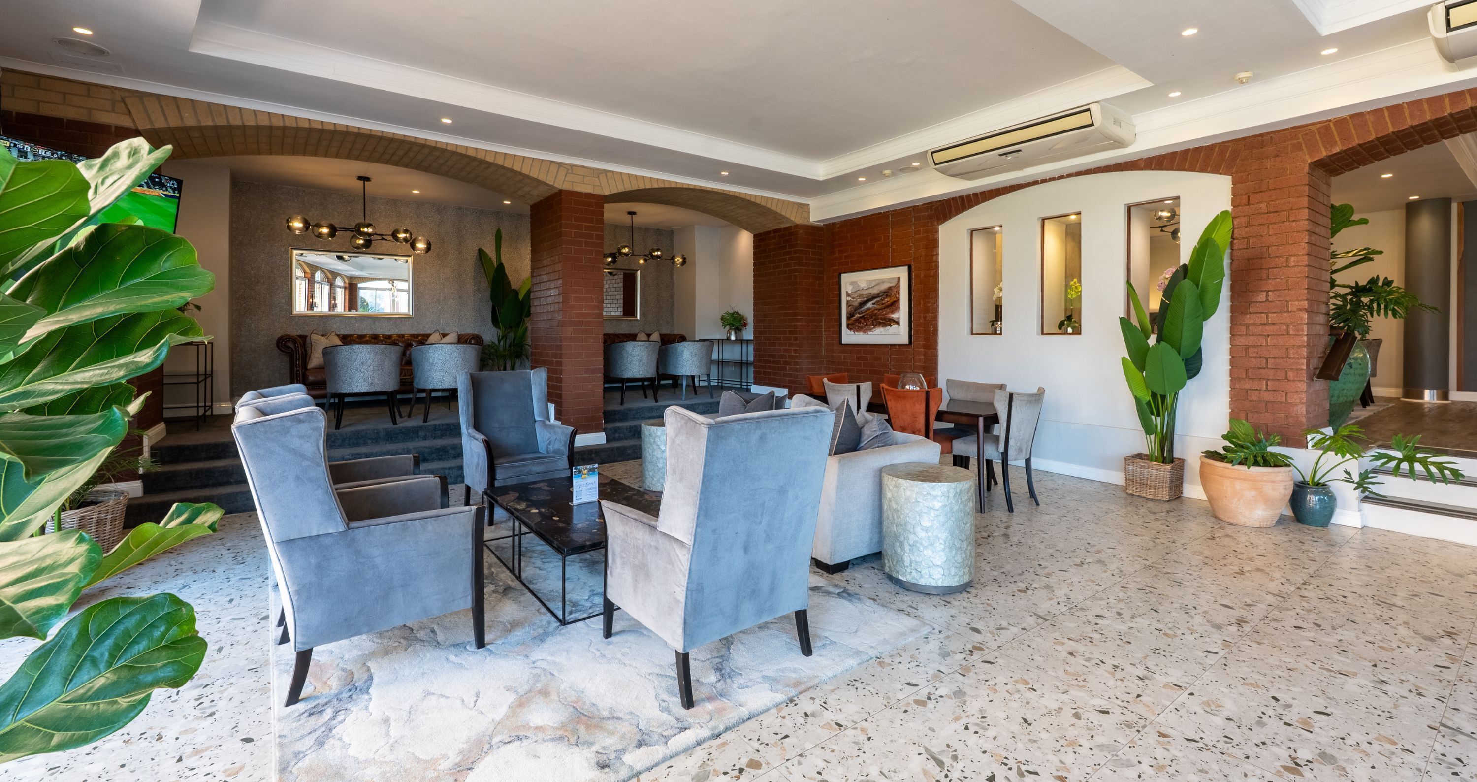 Un vestíbulo amplio con muebles modernos, piso de piedra y grandes plantas en macetas.