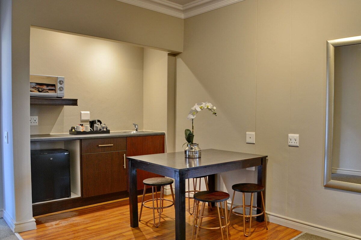 A compact kitchen with a dining table and stools, a refrigerator, and a microwave.