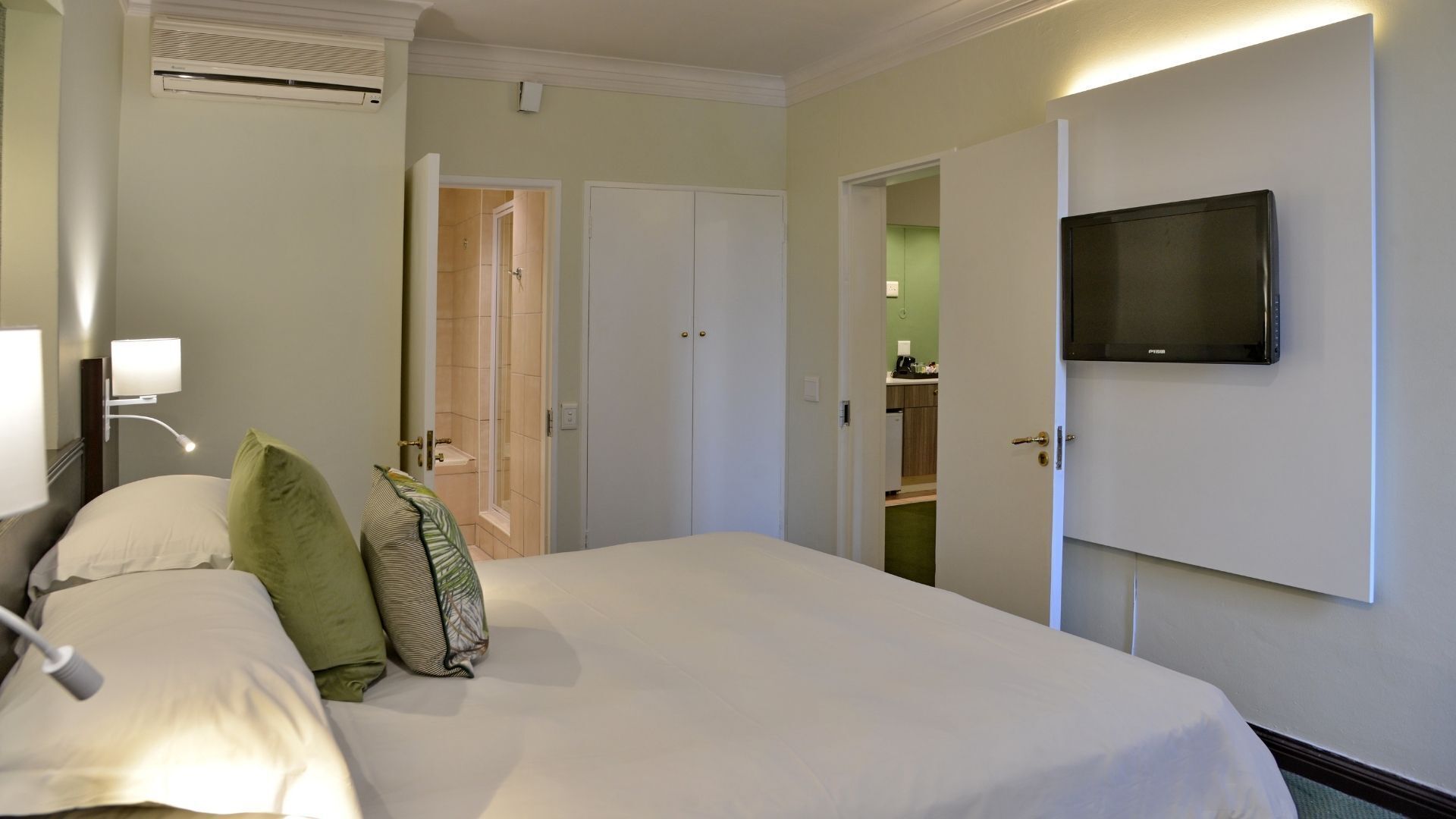 Habitación de hotel con cama, televisión montada en la pared, baño con ducha y kitchenette.
