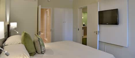 Habitación de hotel con cama, televisión montada en la pared, baño con ducha y kitchenette.