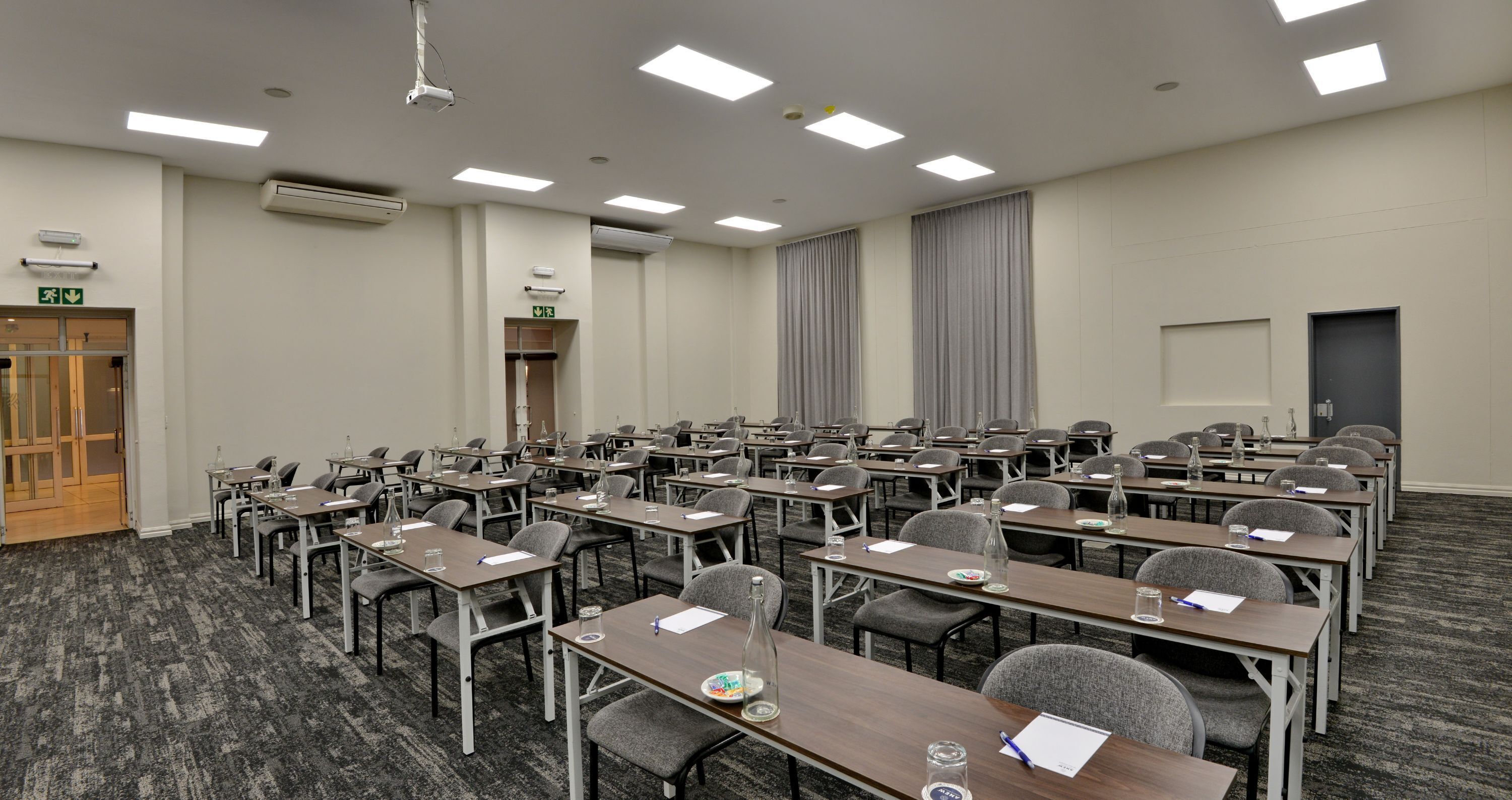 Un salón de conferencias con filas de mesas y sillas, equipado con micrófonos y botellas de agua.