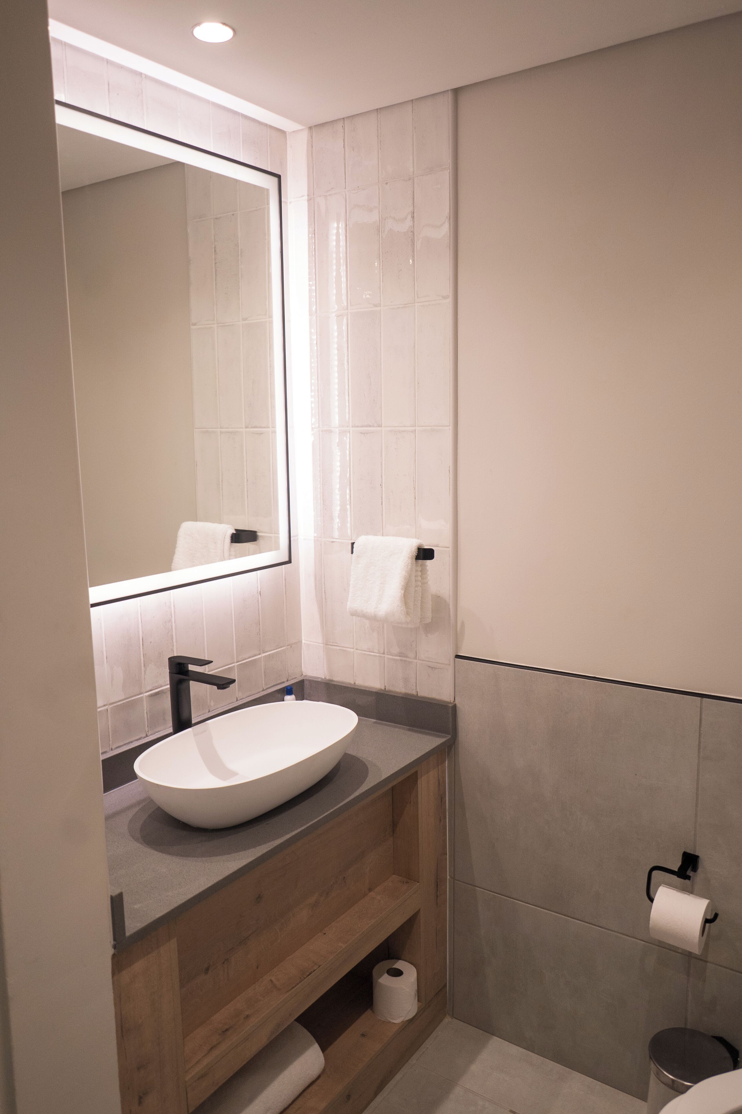 Et moderne badeværelse med et stort spejl, en hvid vask, trækommode og toilet.