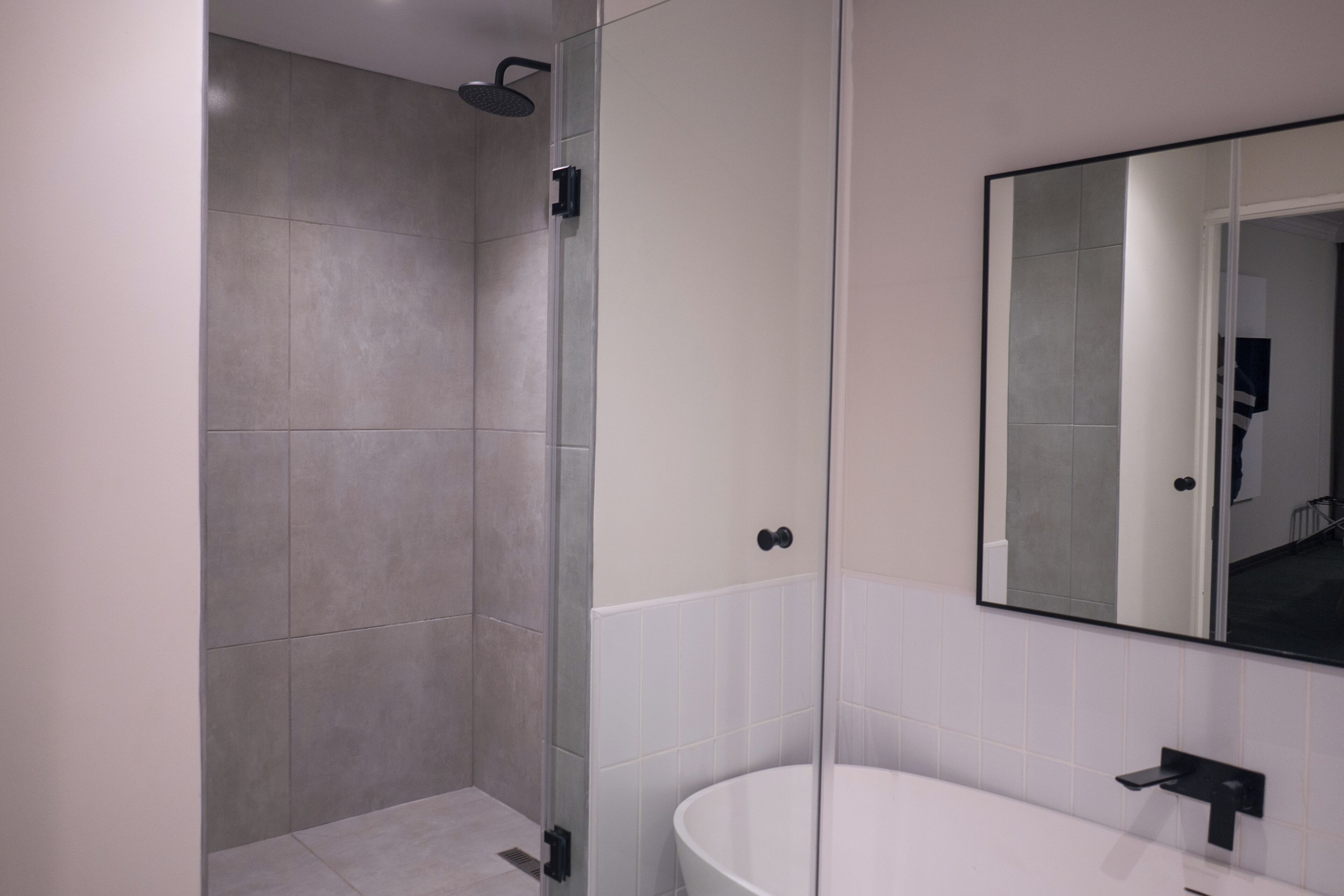 A modern bathroom with a glass shower enclosure, a white bathtub, and a large mirror above the sink.