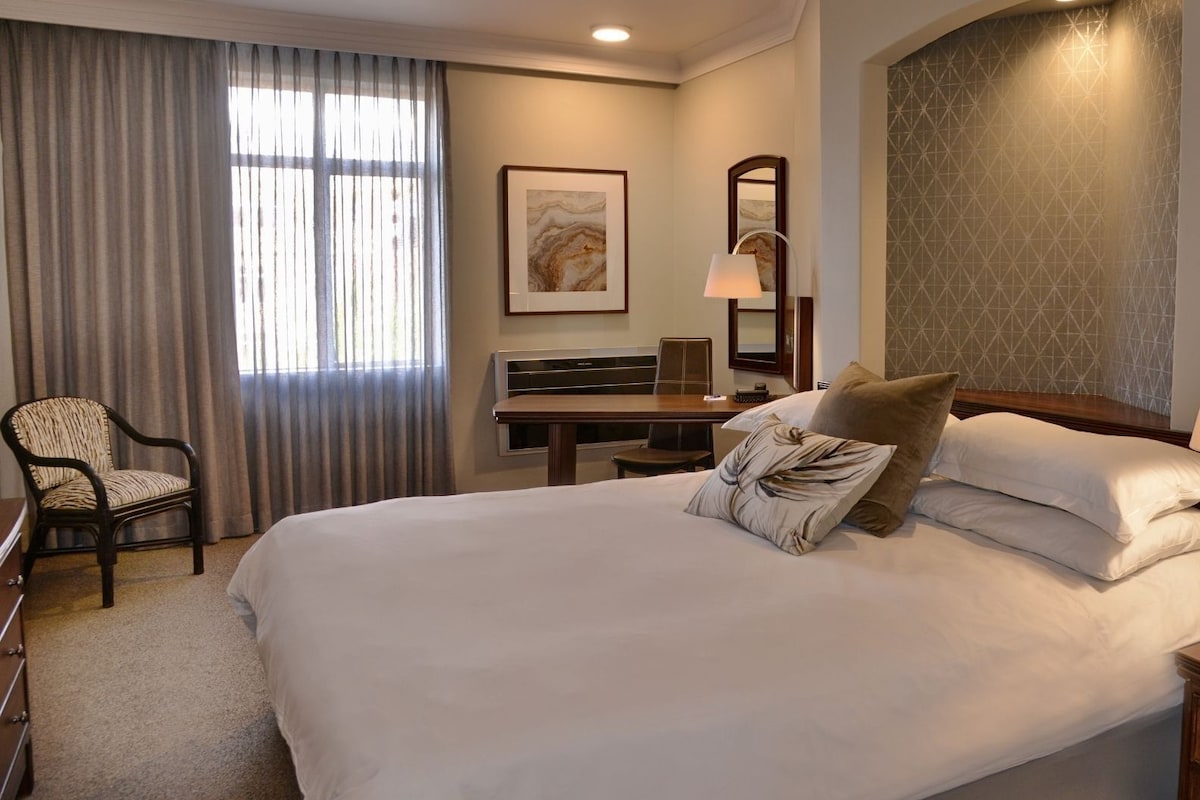 Una habitación de hotel con una cama grande, un escritorio, una silla y una lámpara.