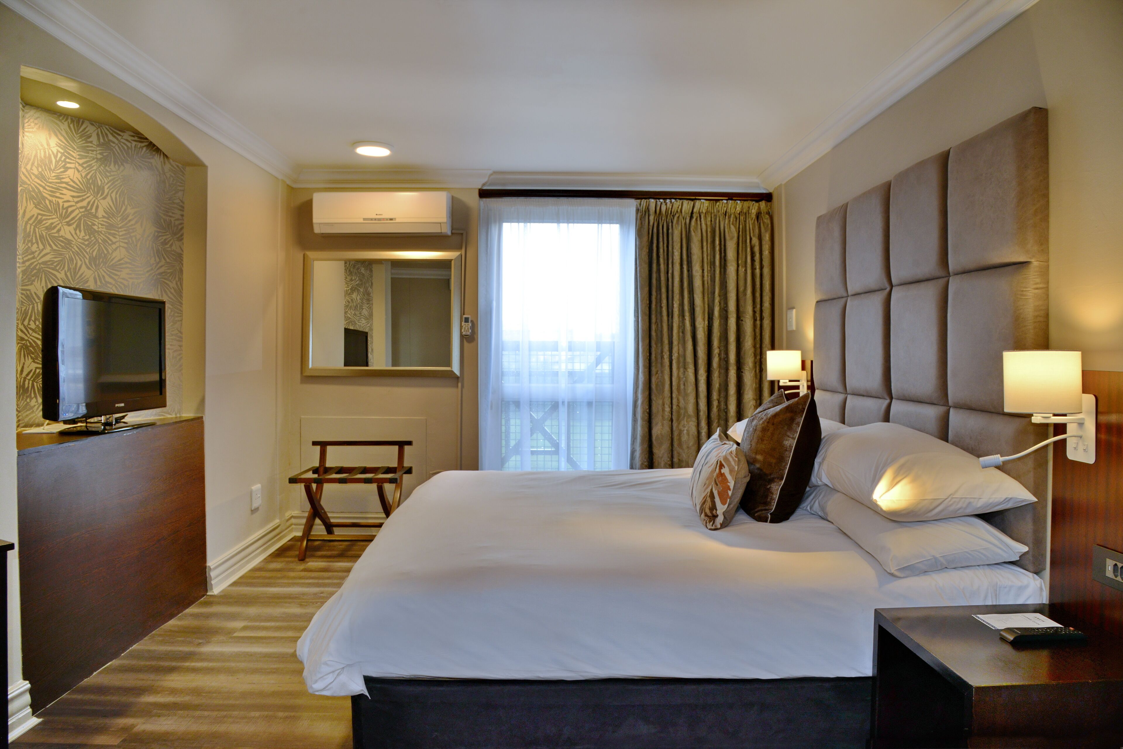 Een hotelkamer met een groot bed, een televisie, een bureau en een raam met gordijnen.