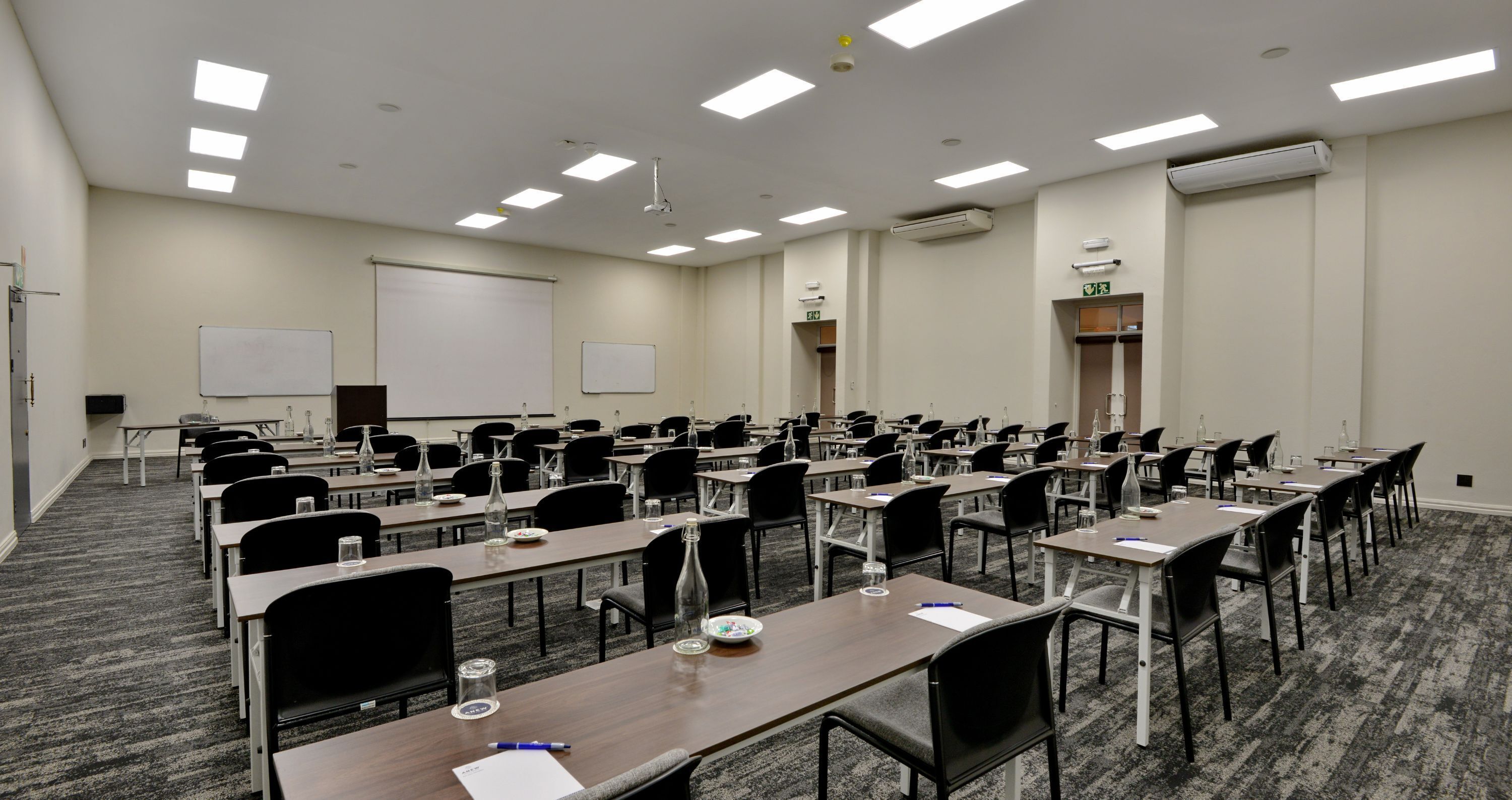 Une salle de conférence équipée de plusieurs tables et chaises, de tableaux blancs et d’un écran de projection.