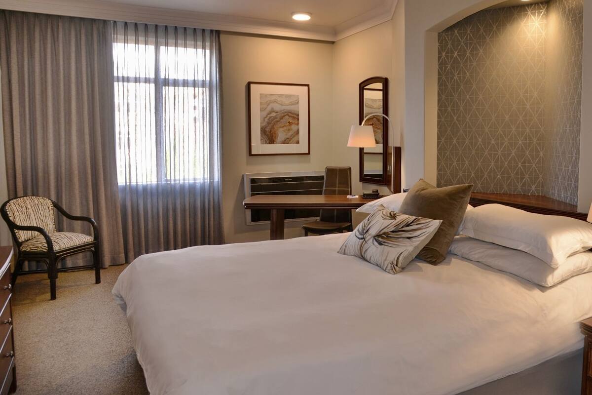 A hotel room with a large bed, a desk, a chair, and a lamp.