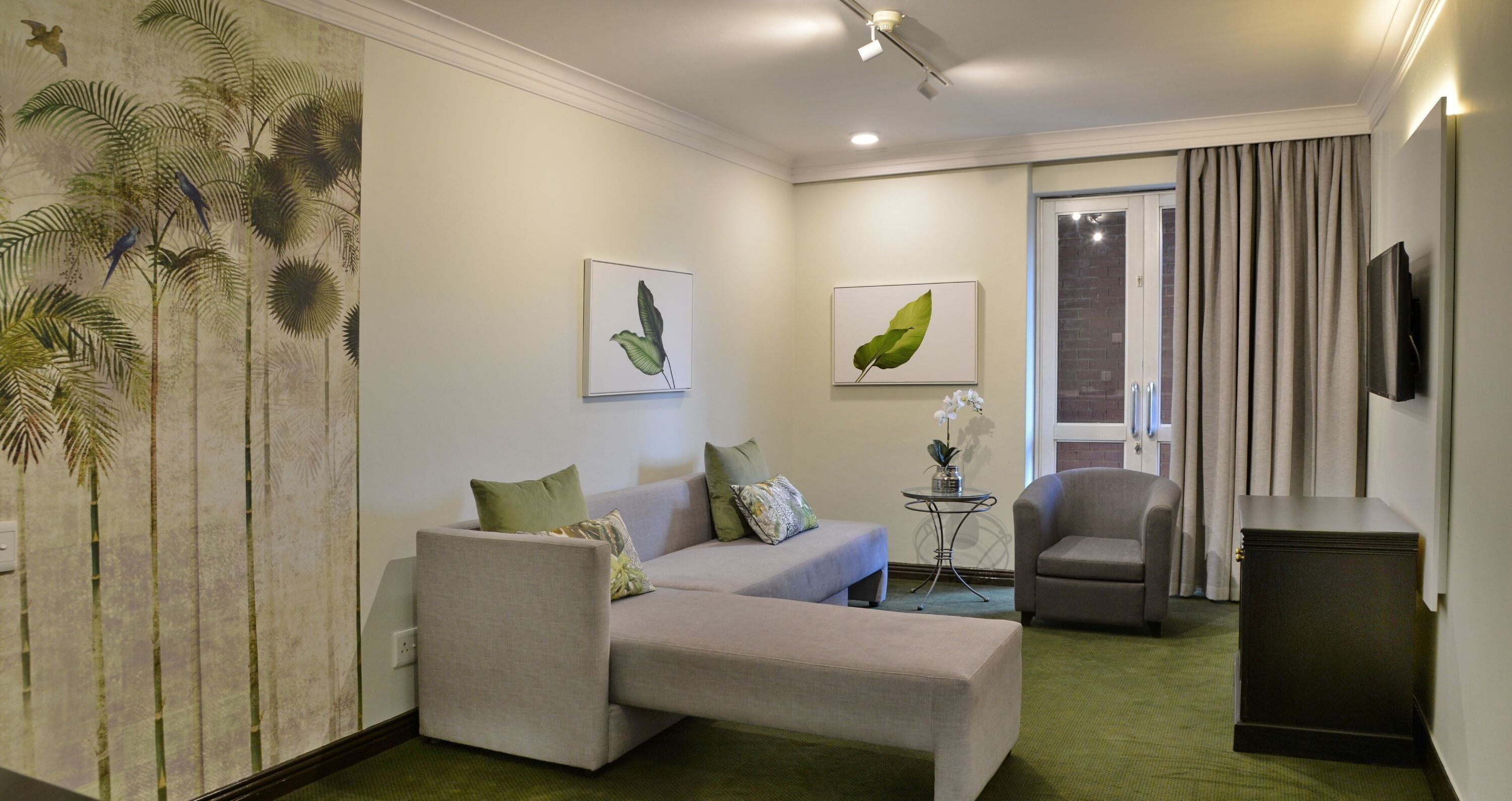 A modern hotel room with a sofa, armchair, and a small table with a plant.