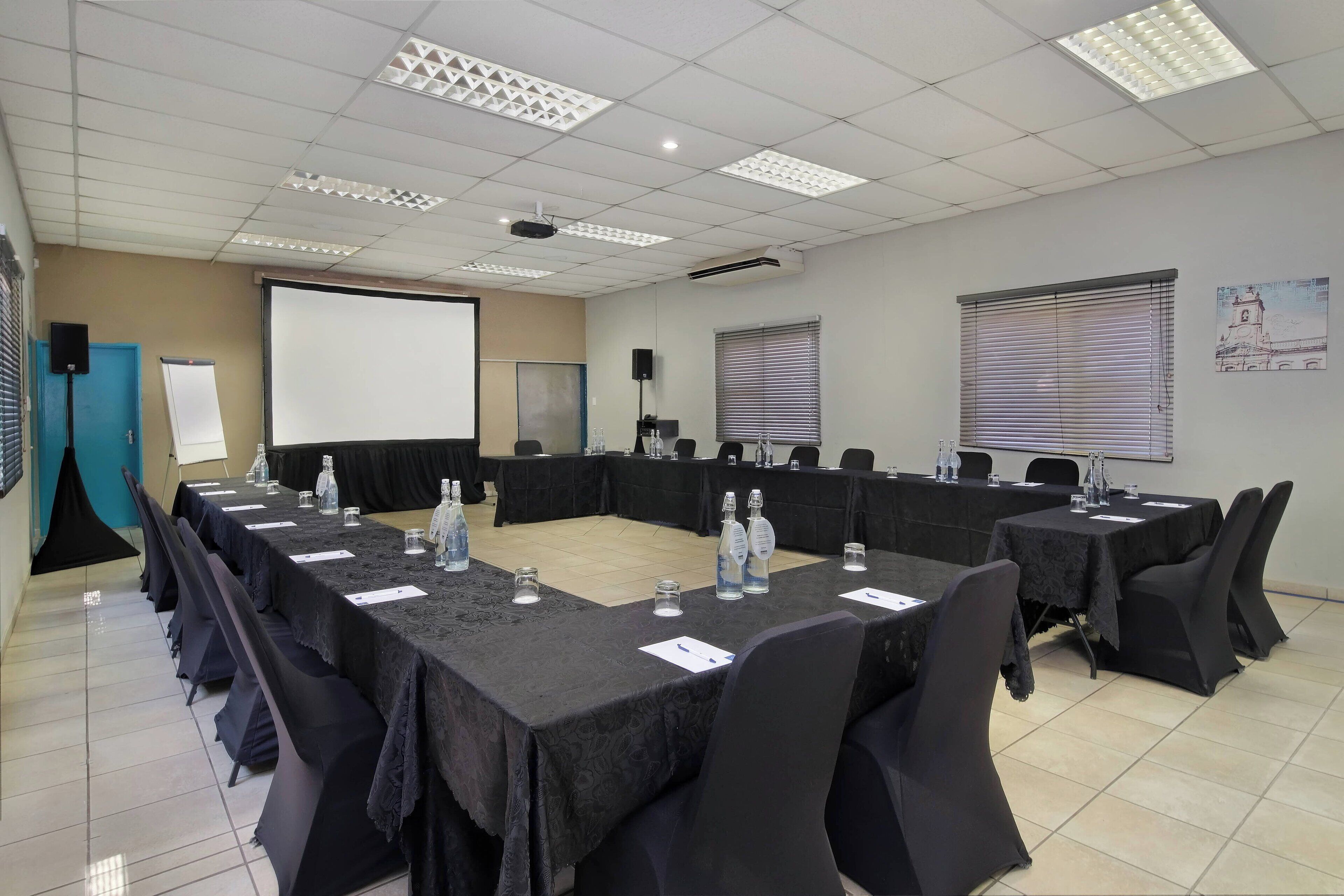 A conference room with a long table, chairs, a projector screen, and a whiteboard.