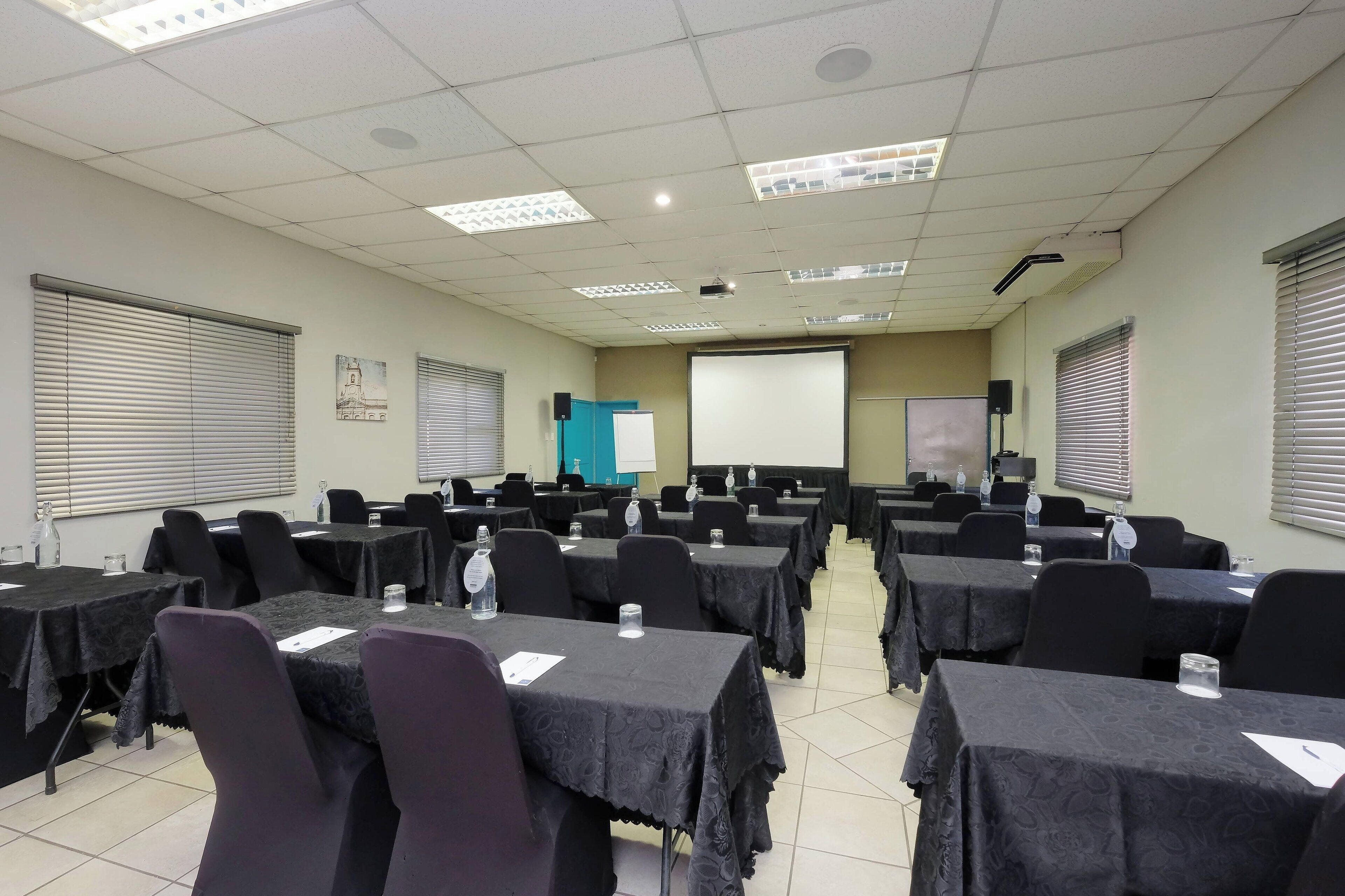 Un salón de conferencias con varias mesas y sillas, equipado con proyectores y pantallas.