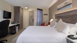 Une chambre d’hôtel avec un grand lit, un bureau avec une chaise, une télévision et un tableau au mur.