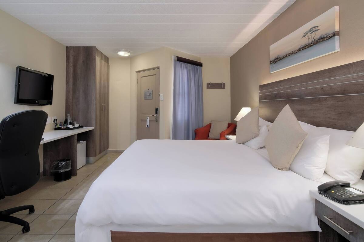 Habitació d'hotel amb un llit gran, una taula de treball amb cadira, televisió i un quadre a la paret.