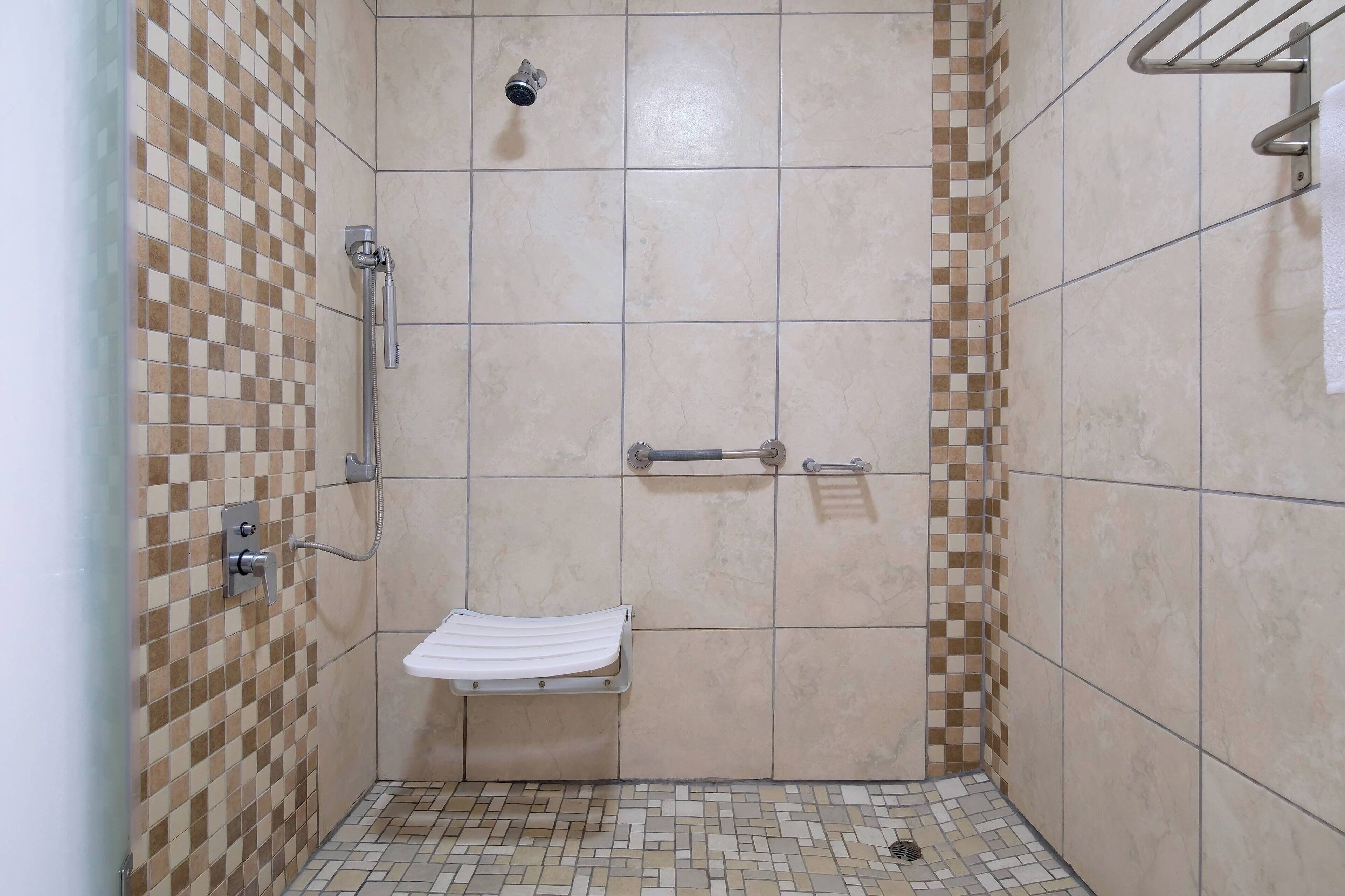 A small, tiled shower area with a bench, grab bars, and a towel rack.