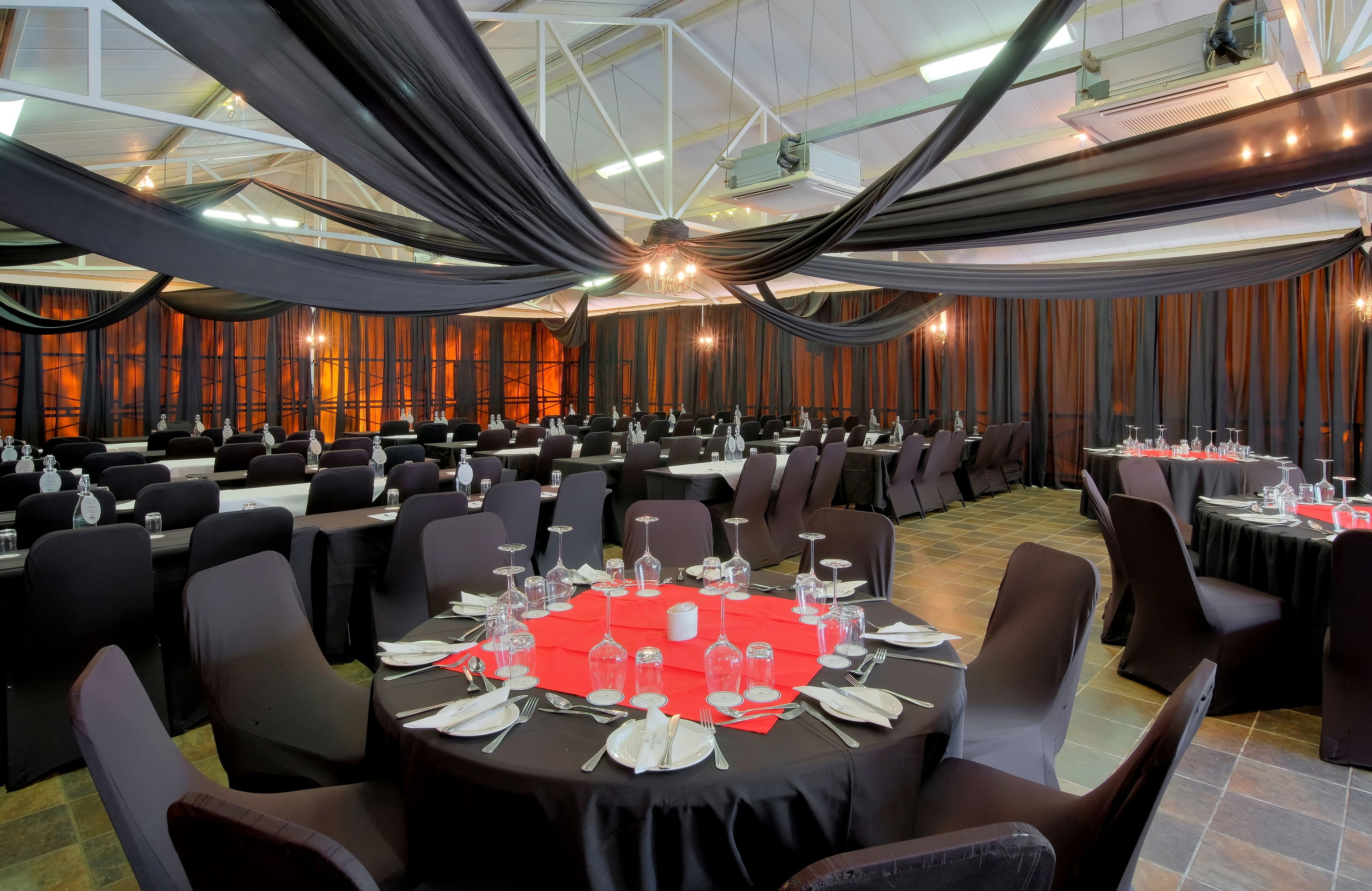 A banquet hall with round tables set for dining, draped with black fabric, and equipped with chairs and dining essentials.