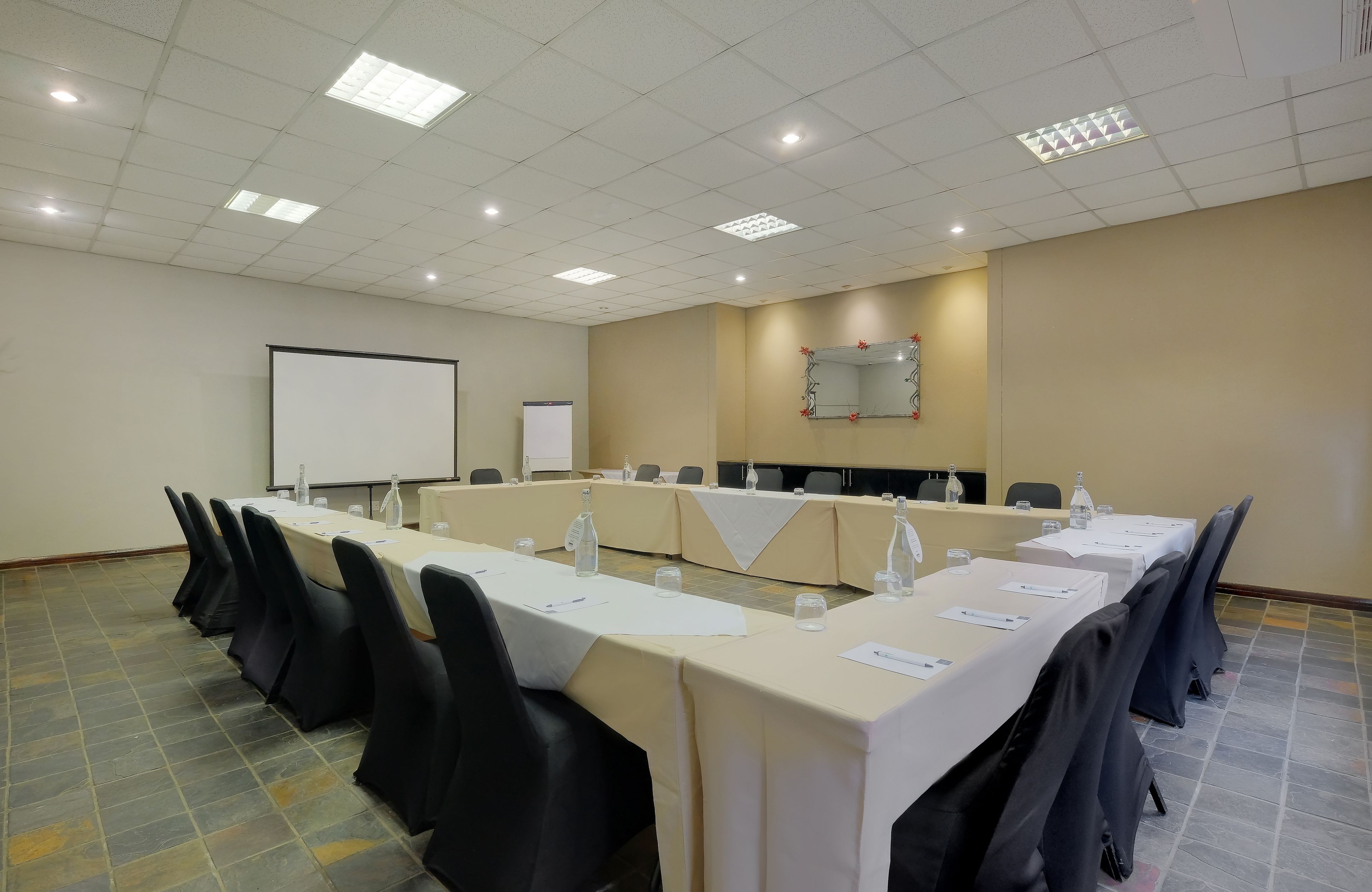 A conference room with a long table, black chairs, a whiteboard, and a projector screen.