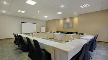 A conference room with a long table, black chairs, a whiteboard, and a projector screen.