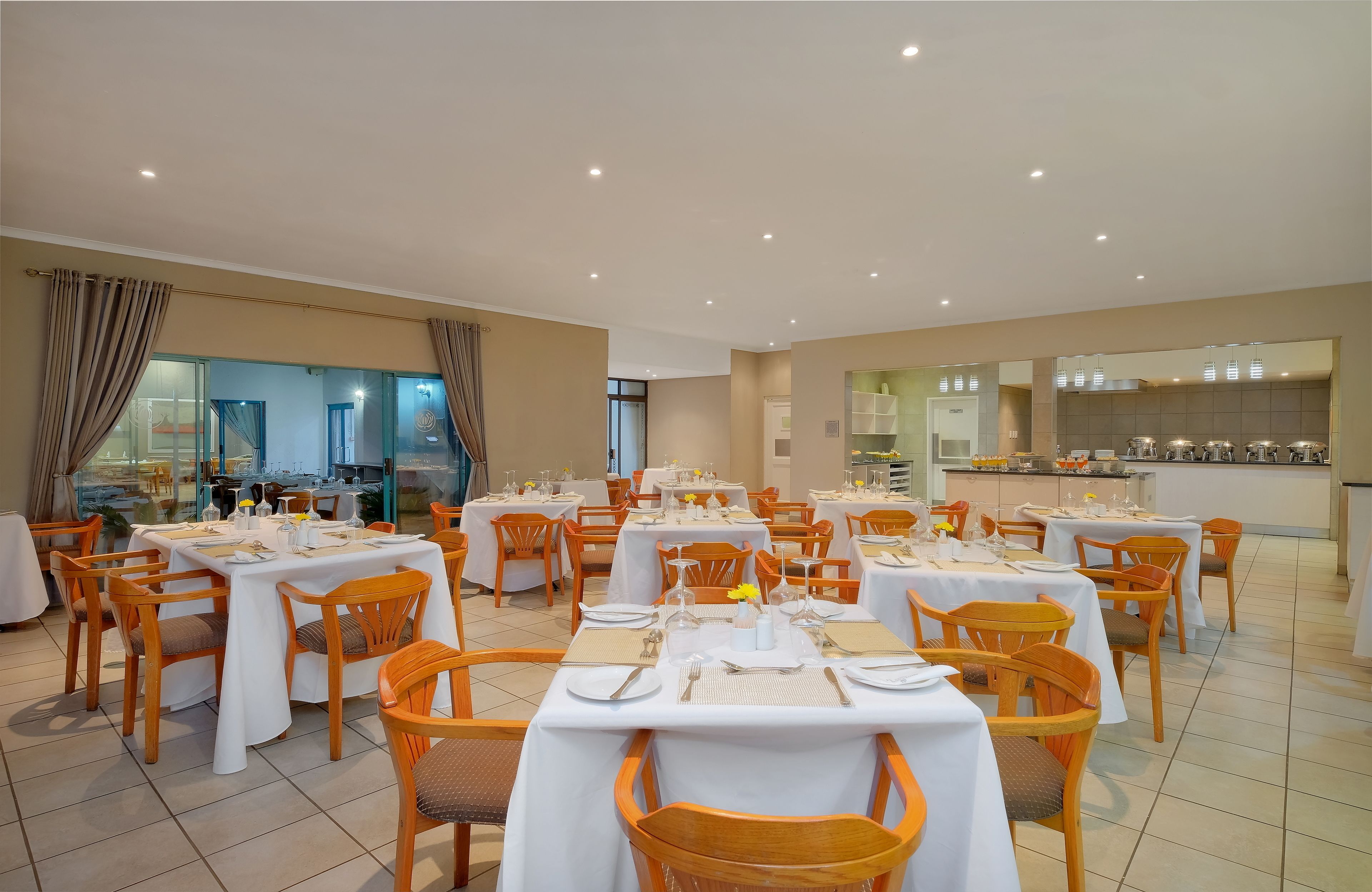 A dining area with multiple tables set for guests, featuring white tablecloths and wooden chairs.