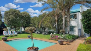 Un espace piscine avec des chaises longues, une terrasse en bois et un bâtiment doté d’un toit végétalisé.