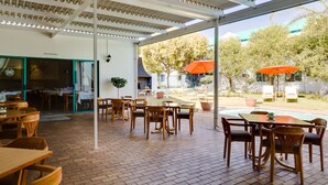 Un espace extérieur aménagé en terrasse, avec des tables et des chaises en bois, une piscine et des parasols orange.