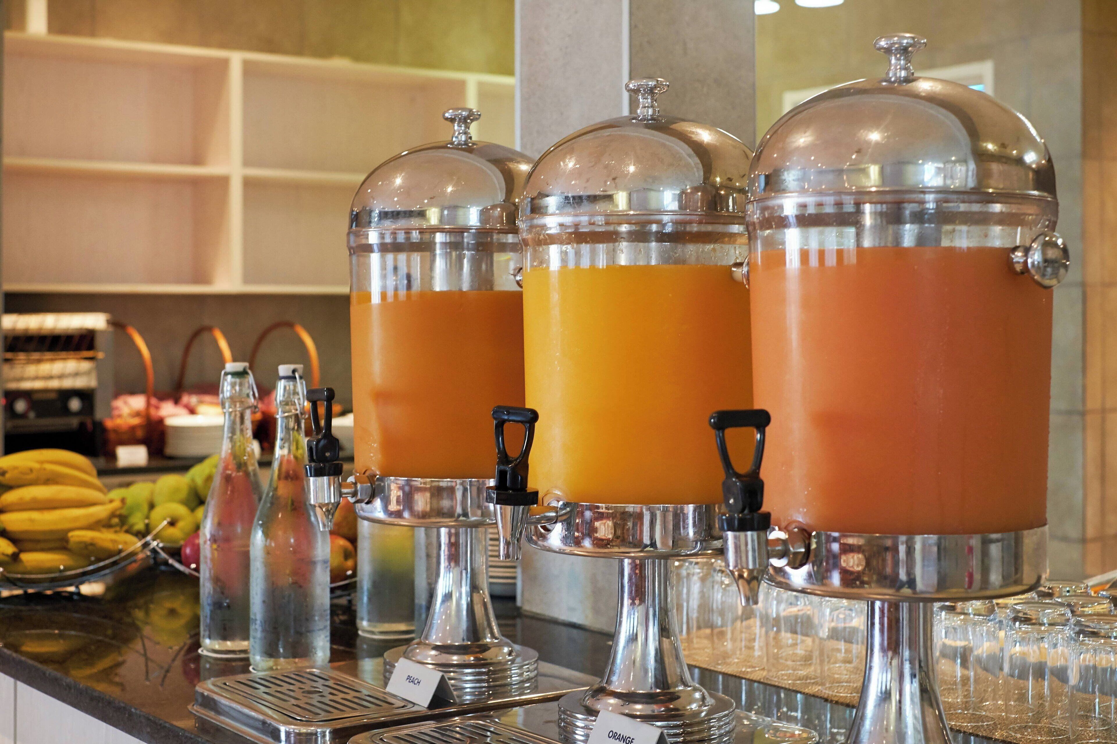 Een buffet met diverse drankdispensers, waaronder jus d'orange en water.
