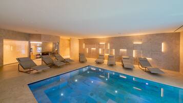 Un área de piscina interior moderna con múltiples tumbonas y una piscina de color azul cristalino.