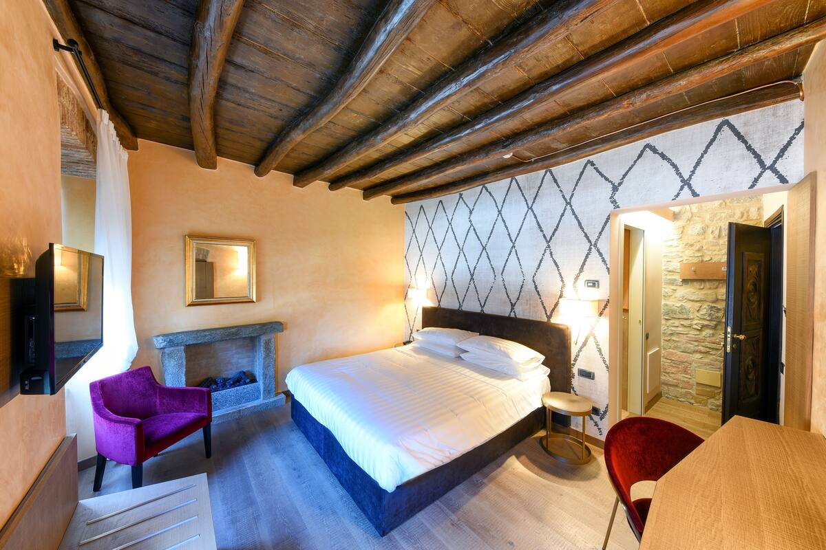 A bedroom with a bed, a fireplace, a stone wall, and a wooden ceiling.