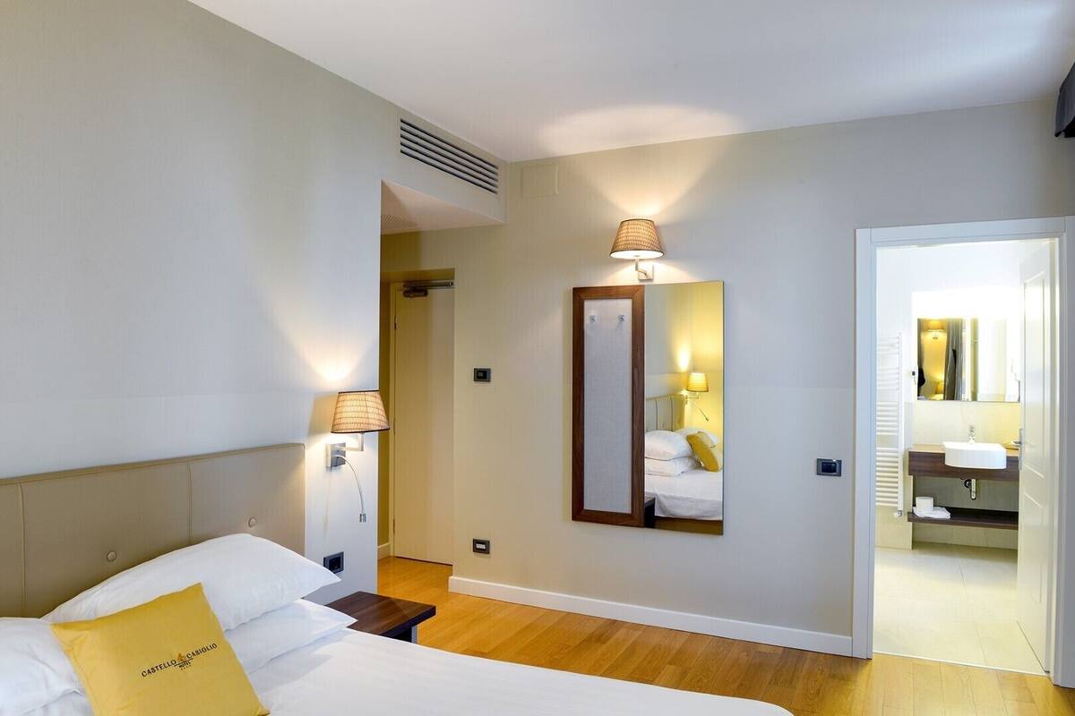 A hotel room with a bed, bedside lamps, a mirror, and a view of the bathroom.
