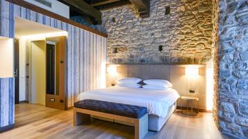 Una camera da letto con parete in pietra, una panca di legno, un letto con biancheria bianca e due lampade ai comodini.