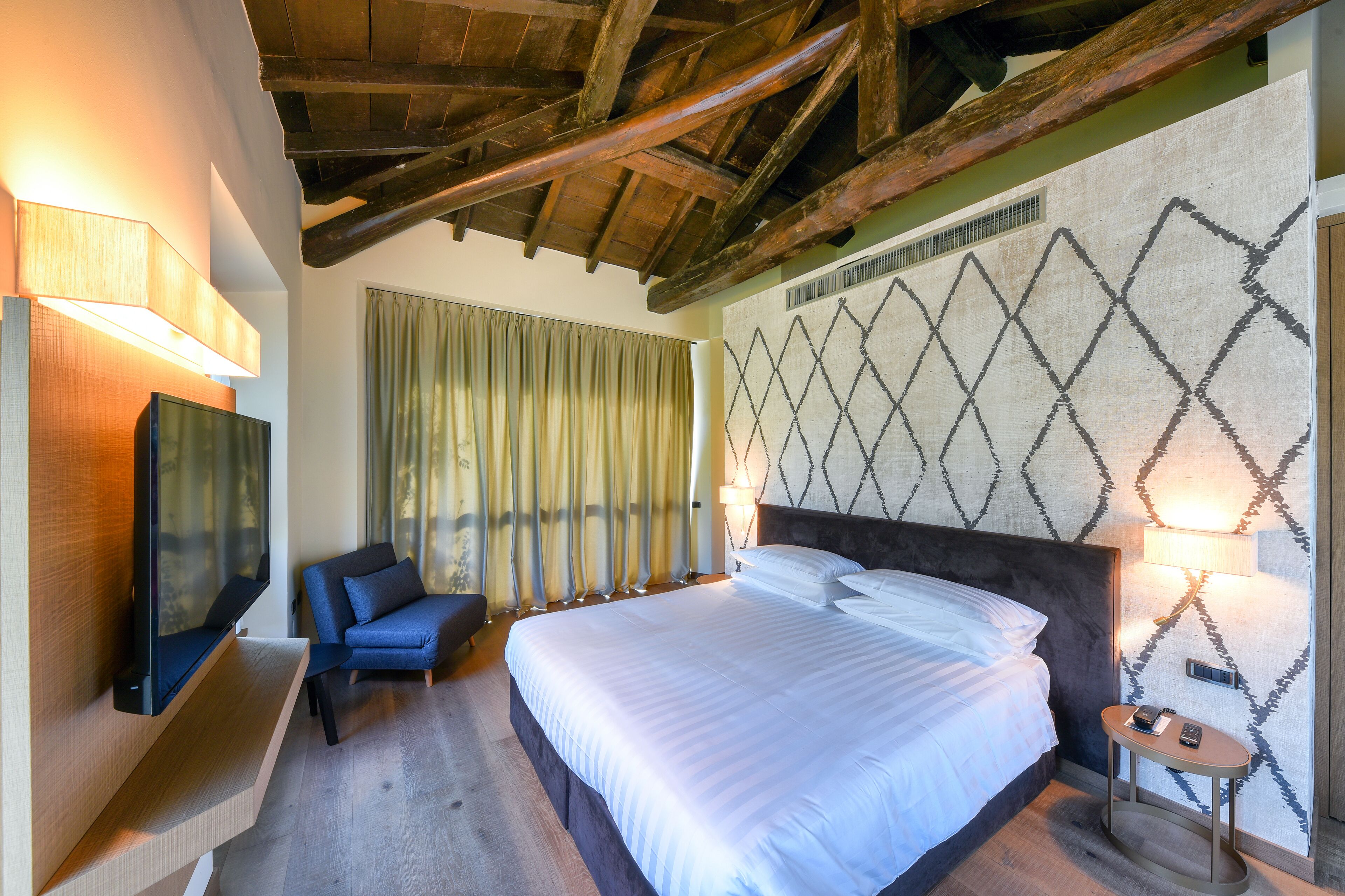 Une chambre d’hôtel avec un grand lit, un téléviseur fixé au mur, une chaise et une table de chevet avec une lampe.