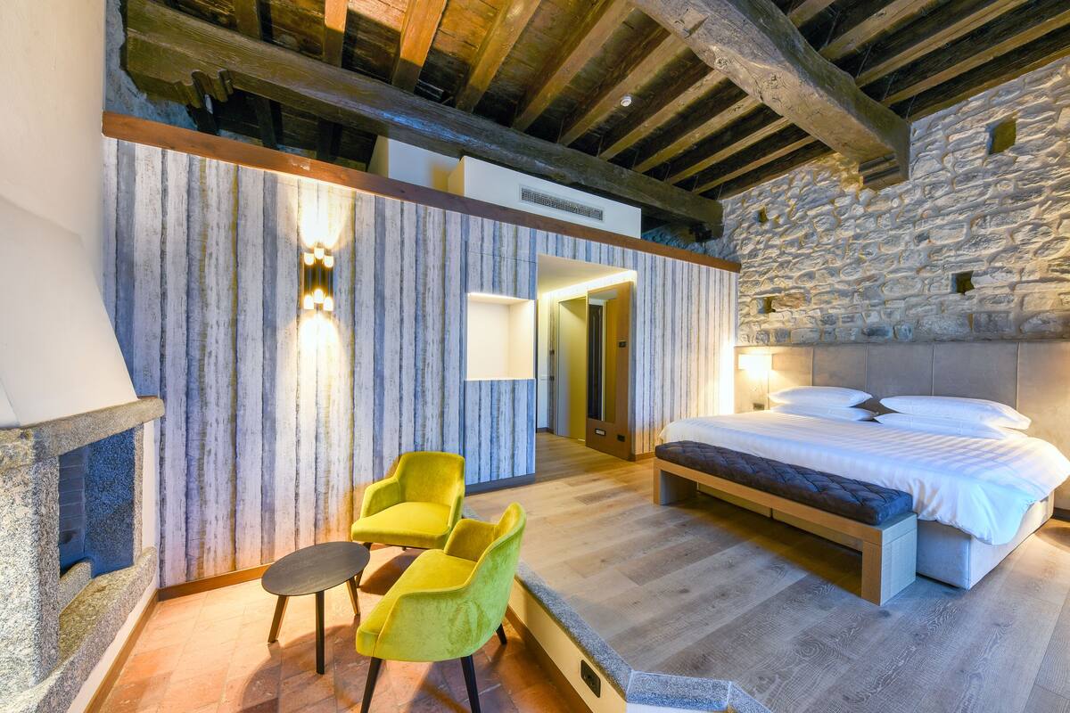 A modern bedroom with a stone wall, a wooden ceiling, a bed, and two yellow chairs.