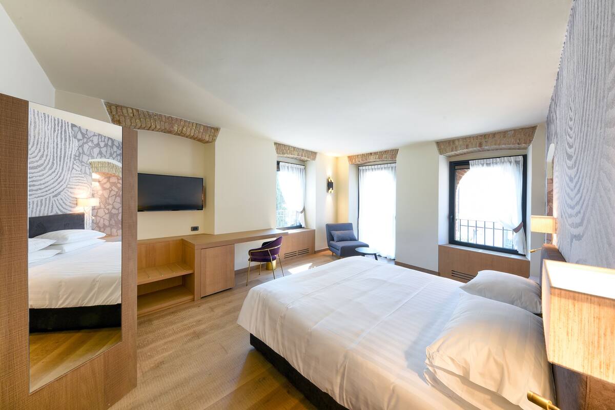 A modern hotel room with a large bed, a desk, a chair, and a TV.