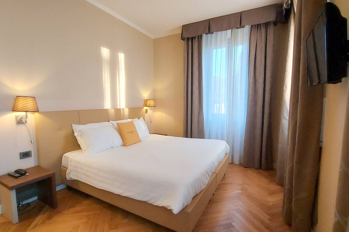 A hotel room with a large bed, two bedside lamps, a bedside table with a phone, and a TV mounted on the wall.