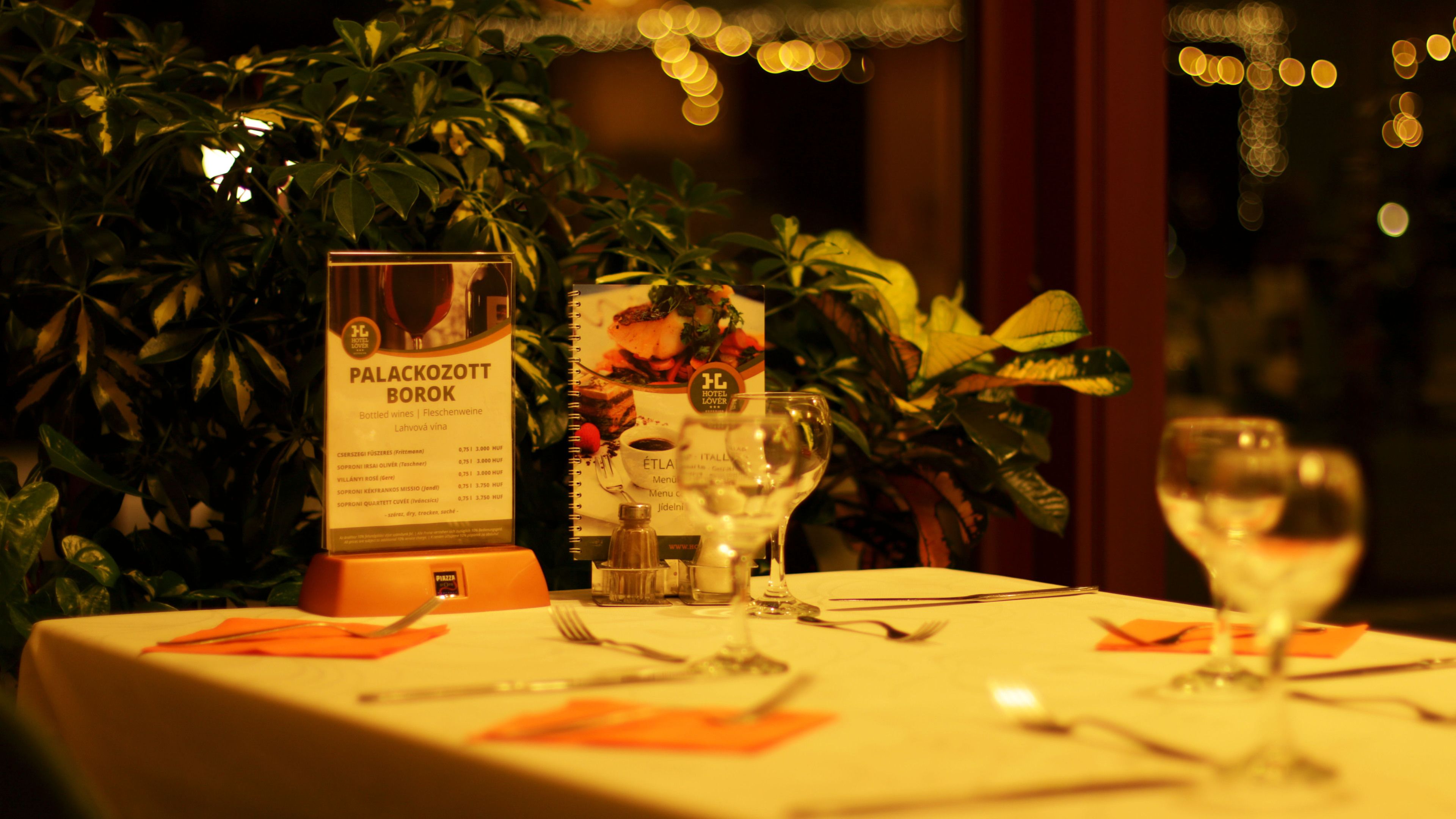 A restaurant table set with a menu, wine glasses, and cutlery.